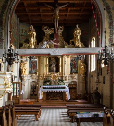 Zdjęcie nr 27: Kościół drewniany, orientowany, jednonawowy o konstrukcji zrębowej, oszalowany. Prezbiterium kwadratowe o wielobocznym zamknięciu z zakrystią od północy. Nawa szersza, prawie kwadratowa, przy niej od północy kaplica i składzik później dostawiony; od południa i od zachodu kruchty. Korpus nakryty dachem dwuspadowym, jednokalenicowym, z barokową wieżyczką na sygnaturkę na kalenicy; składzik nakryty dachem pulpitowym. Wewnątrz stropy kasetonowe. Otwór tęczy o profilowanym łuku półkolistym podwyższonym; belka profilowana, na niej grupa Ukrzyżowania. Chór muzyczny wsparty na dwóch słupach. Kaplica otwarta do nawy półkolistą arkadą. Troje drzwi o ozdobnych obramieniach uszatych, schodkowatych i uszato-schodkowatych, ze starymi okuciami. Wieża nowa, izbicowa o pochyłych ścianach, zwieńczona ostrosłupowym hełmem.
