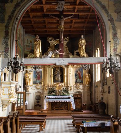 Zdjęcie nr 28: Kościół drewniany, orientowany, jednonawowy o konstrukcji zrębowej, oszalowany. Prezbiterium kwadratowe o wielobocznym zamknięciu z zakrystią od północy. Nawa szersza, prawie kwadratowa, przy niej od północy kaplica i składzik później dostawiony; od południa i od zachodu kruchty. Korpus nakryty dachem dwuspadowym, jednokalenicowym, z barokową wieżyczką na sygnaturkę na kalenicy; składzik nakryty dachem pulpitowym. Wewnątrz stropy kasetonowe. Otwór tęczy o profilowanym łuku półkolistym podwyższonym; belka profilowana, na niej grupa Ukrzyżowania. Chór muzyczny wsparty na dwóch słupach. Kaplica otwarta do nawy półkolistą arkadą. Troje drzwi o ozdobnych obramieniach uszatych, schodkowatych i uszato-schodkowatych, ze starymi okuciami. Wieża nowa, izbicowa o pochyłych ścianach, zwieńczona ostrosłupowym hełmem.
