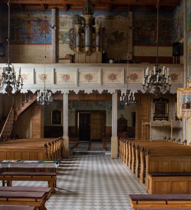 Zdjęcie nr 33: Kościół drewniany, orientowany, jednonawowy o konstrukcji zrębowej, oszalowany. Prezbiterium kwadratowe o wielobocznym zamknięciu z zakrystią od północy. Nawa szersza, prawie kwadratowa, przy niej od północy kaplica i składzik później dostawiony; od południa i od zachodu kruchty. Korpus nakryty dachem dwuspadowym, jednokalenicowym, z barokową wieżyczką na sygnaturkę na kalenicy; składzik nakryty dachem pulpitowym. Wewnątrz stropy kasetonowe. Otwór tęczy o profilowanym łuku półkolistym podwyższonym; belka profilowana, na niej grupa Ukrzyżowania. Chór muzyczny wsparty na dwóch słupach. Kaplica otwarta do nawy półkolistą arkadą. Troje drzwi o ozdobnych obramieniach uszatych, schodkowatych i uszato-schodkowatych, ze starymi okuciami. Wieża nowa, izbicowa o pochyłych ścianach, zwieńczona ostrosłupowym hełmem.
