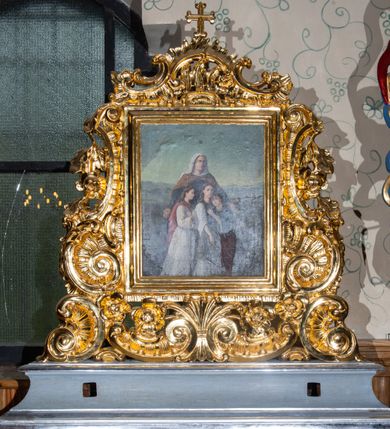 Zdjęcie nr 17: Feretron dwustronny z obrazami św. Zofii i św. Barbary, ustawiony na prostopadłościennej, profilowanej podstawie o wklęsłym przebiegu, zaopatrzonej w otwory na drążki do noszenia. Rama obrazów w kształcie stojącego prostokąta, obwiedziona bogatą dekoracją rokokową z rocaille’ami i kwiatami, zwieńczona niewielkim łacińskim krzyżykiem. Po jednej stronie obraz przedstawiający św. Zofię i stojące przed nią trzy córki. Święta zwrócona delikatnie w lewo, z szeroko rozłożonymi rękami na boki. Twarz owalna o delikatnych rysach. Ubrana jest w długą, ciemną suknię, brązowy płaszcz spięty pod szyją i biały welon. Nad głową świętej złoty i okrągły nimb. Dwie córki od lewej strony zwrócone trzy czwarte w lewo. Ubrane w długie jasne suknie, córka po lewej dodatkowo w czerwony płaszcz i z małym krzyżykiem w dłoni, a córka po środku w zielony fartuch i kij w prawej dłoni. Córka po prawej, zwrócona w prawo, oparta o ramię siostry, z lewą ręką opartą o nią. Ubrana jest w fioletową spódnicę i niebieską bluzkę z szerokimi rękawami. Twarze córek o delikatnych rysach, okolone długimi i ciemnobrązowymi włosami. W tle oddalony górski krajobraz, w górze błękitne niebo. Po drugiej stronie obrazu przedstawienie św. Barbary. W centrum święta ujęta do kolan, ukazana frontalnie, z głową zwróconą w prawo i przechyloną do tyłu, ze wzrokiem skierowanym ku górze. W prawej dłoni trzyma kielich z hostią, w lewej, opuszczonej gałązka palmy i miecz skierowany ostrzem w dół. Twarz pełna, o dużych oczach, prostym nosie i szerokich ustach. Święta jest ubrana w żółtą suknię oraz niebieski płaszcz; na głowie ma założoną zieloną chusteczkę, spod której widać długie, jasne i kręcone włosy. Po prawej stronie obrazu wysoka wieża, tło jednolite, szare, rozświetlone w górnej lewej części obrazu.