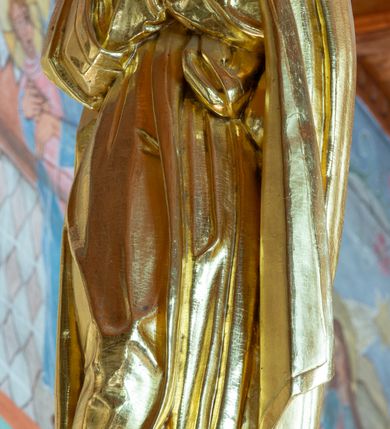 Zdjęcie nr 3: Łuk tęczowy o półkolistym wykroju, na profilowanej belce zdobionej pośrodku ryzowaną rozetą ustawiona grupa Ukrzyżowania. W centrum krucyfiks, po prawej św. Jan Ewangelista, po lewej Matka Boska i św. Maria Magdalena obejmująca krzyż. Chrystus przybity do krzyża trzema gwoździami, sylwetka w delikatnym zwisie, z głową pochyloną delikatnie w dół, o sztywnym układzie sylwetki z zaznaczonymi śladami męki. Perizonium w formie tkaniny przewiązanej na prawym biodrze ze zwisem wzdłuż prawego uda. Twarz podłużna, okolona zarostem; włosy długie spływające na prawe ramię w silnie skręcone pukle, na głowie zielona korona cierniowa złożona z dwóch przeplatających się gałązek. Nad głową Chrystusa biały titulus z napisem: „I(ESUS) N(AZARENUS) R(EX) I(UDAEORUM)”. Krzyż prosty, gładki o ramionach zakończonych gzymsikami. Po lewej stronie krucyfiksu rzeźba św. Marii Magdaleny ukazana w pozycji klęczącej, pochylonej do przodu, obejmująca dłońmi krzyż. Święta jest ubrana w długą, srebrzoną suknię, odsłaniającą nagie ramiona, przewiązaną w talii. Twarz szeroka, delikatnie otwarte usta, małe oczy i długi nos. Głowę okalają długie, ciemne włosy, spływające na plecy. Za nią ustawiona jest rzeźba Matki Boskiej w delikatnym kontrapoście, z prawą nogą ugiętą w kolanie, ze splecionymi na wysokości piersi rękami. Maria jest ubrana w długą, złoconą suknię oraz złocony płaszcz założony na głowę i spływający wzdłuż sylwetki. Twarz szeroka, z wyraźnie zaznaczonym podbródkiem, wzrok skierowany na krucyfiks, zmarszczone brwi. Po prawej stronie rzeźba św. Jana Ewangelisty, ukazanego w postawie stojącej, zwróconego w trzech czwartych w prawo, z rękami splecionymi na wysokości pasa. Twarz owalna, małe usta, długi i wąski nos, wzrok skierowany ku górze, zmarszczone brwi. Włosy ciemne, bujne, spływające na plecy. Święty ubrany jest w długą, złoconą suknię z długimi rękawami. Rzeźby ustawione są na niskich, zielonych cokolikach. Polichromia w odsłoniętych partiach ciała naturalistyczna, detale złocone i srebrzone. 
