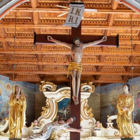 Zdjęcie nr 1: Łuk tęczowy o półkolistym wykroju, na profilowanej belce zdobionej pośrodku ryzowaną rozetą ustawiona grupa Ukrzyżowania. W centrum krucyfiks, po prawej św. Jan Ewangelista, po lewej Matka Boska i św. Maria Magdalena obejmująca krzyż. Chrystus przybity do krzyża trzema gwoździami, sylwetka w delikatnym zwisie, z głową pochyloną delikatnie w dół, o sztywnym układzie sylwetki z zaznaczonymi śladami męki. Perizonium w formie tkaniny przewiązanej na prawym biodrze ze zwisem wzdłuż prawego uda. Twarz podłużna, okolona zarostem; włosy długie spływające na prawe ramię w silnie skręcone pukle, na głowie zielona korona cierniowa złożona z dwóch przeplatających się gałązek. Nad głową Chrystusa biały titulus z napisem: „I(ESUS) N(AZARENUS) R(EX) I(UDAEORUM)”. Krzyż prosty, gładki o ramionach zakończonych gzymsikami. Po lewej stronie krucyfiksu rzeźba św. Marii Magdaleny ukazana w pozycji klęczącej, pochylonej do przodu, obejmująca dłońmi krzyż. Święta jest ubrana w długą, srebrzoną suknię, odsłaniającą nagie ramiona, przewiązaną w talii. Twarz szeroka, delikatnie otwarte usta, małe oczy i długi nos. Głowę okalają długie, ciemne włosy, spływające na plecy. Za nią ustawiona jest rzeźba Matki Boskiej w delikatnym kontrapoście, z prawą nogą ugiętą w kolanie, ze splecionymi na wysokości piersi rękami. Maria jest ubrana w długą, złoconą suknię oraz złocony płaszcz założony na głowę i spływający wzdłuż sylwetki. Twarz szeroka, z wyraźnie zaznaczonym podbródkiem, wzrok skierowany na krucyfiks, zmarszczone brwi. Po prawej stronie rzeźba św. Jana Ewangelisty, ukazanego w postawie stojącej, zwróconego w trzech czwartych w prawo, z rękami splecionymi na wysokości pasa. Twarz owalna, małe usta, długi i wąski nos, wzrok skierowany ku górze, zmarszczone brwi. Włosy ciemne, bujne, spływające na plecy. Święty ubrany jest w długą, złoconą suknię z długimi rękawami. Rzeźby ustawione są na niskich, zielonych cokolikach. Polichromia w odsłoniętych partiach ciała naturalistyczna, detale złocone i srebrzone. 
