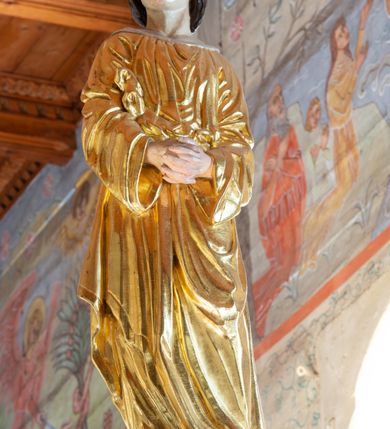 Zdjęcie nr 11: Łuk tęczowy o półkolistym wykroju, na profilowanej belce zdobionej pośrodku ryzowaną rozetą ustawiona grupa Ukrzyżowania. W centrum krucyfiks, po prawej św. Jan Ewangelista, po lewej Matka Boska i św. Maria Magdalena obejmująca krzyż. Chrystus przybity do krzyża trzema gwoździami, sylwetka w delikatnym zwisie, z głową pochyloną delikatnie w dół, o sztywnym układzie sylwetki z zaznaczonymi śladami męki. Perizonium w formie tkaniny przewiązanej na prawym biodrze ze zwisem wzdłuż prawego uda. Twarz podłużna, okolona zarostem; włosy długie spływające na prawe ramię w silnie skręcone pukle, na głowie zielona korona cierniowa złożona z dwóch przeplatających się gałązek. Nad głową Chrystusa biały titulus z napisem: „I(ESUS) N(AZARENUS) R(EX) I(UDAEORUM)”. Krzyż prosty, gładki o ramionach zakończonych gzymsikami. Po lewej stronie krucyfiksu rzeźba św. Marii Magdaleny ukazana w pozycji klęczącej, pochylonej do przodu, obejmująca dłońmi krzyż. Święta jest ubrana w długą, srebrzoną suknię, odsłaniającą nagie ramiona, przewiązaną w talii. Twarz szeroka, delikatnie otwarte usta, małe oczy i długi nos. Głowę okalają długie, ciemne włosy, spływające na plecy. Za nią ustawiona jest rzeźba Matki Boskiej w delikatnym kontrapoście, z prawą nogą ugiętą w kolanie, ze splecionymi na wysokości piersi rękami. Maria jest ubrana w długą, złoconą suknię oraz złocony płaszcz założony na głowę i spływający wzdłuż sylwetki. Twarz szeroka, z wyraźnie zaznaczonym podbródkiem, wzrok skierowany na krucyfiks, zmarszczone brwi. Po prawej stronie rzeźba św. Jana Ewangelisty, ukazanego w postawie stojącej, zwróconego w trzech czwartych w prawo, z rękami splecionymi na wysokości pasa. Twarz owalna, małe usta, długi i wąski nos, wzrok skierowany ku górze, zmarszczone brwi. Włosy ciemne, bujne, spływające na plecy. Święty ubrany jest w długą, złoconą suknię z długimi rękawami. Rzeźby ustawione są na niskich, zielonych cokolikach. Polichromia w odsłoniętych partiach ciała naturalistyczna, detale złocone i srebrzone. 
