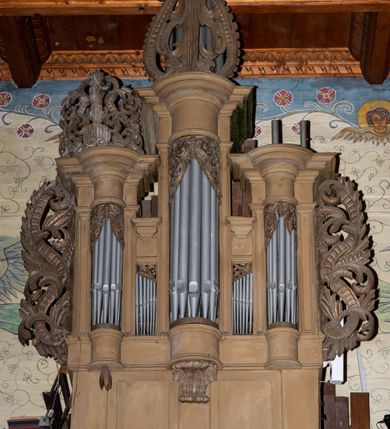 Zdjęcie nr 2: Organy architektoniczne, pięcioosiowe na wysokiej podstawie i niewielkim cokole, trójwieżyczkowe. Wieżyczki boczne niższe od środkowej, wszystkie z półokrągłymi ryzalitami, z prostokątnymi i wypukłymi prześwitami na piszczałki, dekorowanymi w górnych narożach akantem, zakończone fryzem i gzymsem oraz ornamentalnymi szczytami utworzonymi z akantu, karbowanej wstęgi, kampanul i muszli; ryzality u spodu z podwieszonymi kampanulami i muszlą. Szczyt środkowej wieżyczki utworzony z ornamentu małżowinowo-chrząstkowego. Pomiędzy wieżyczkami dwie najniższe osie z prześwitami na piszczałki w formie stojącego prostokąta, zakończone fragmentami gzymsu. Organy ujęte uszami utworzonymi z akantu i karbowanej wstęgi. Struktura polichromowana w całości w kolorze ciemnobeżowym, ornamenty złocone.