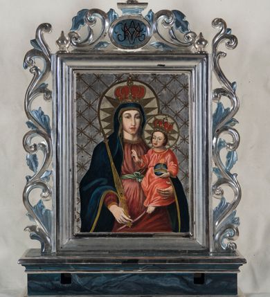 Zdjęcie nr 3: Feretron uzyskał kształt stojącego prostokąta. Tworzy go dwustronnie malowany na płótnie obraz, ujęty w profilowane, srebrzone ramy, ustawiony na postumencie. Ma on formę podłużnego prostopadłościanu, dekorowanego w dolnej i górnej części profilowanymi i srebrzonymi listwami. Dodatkowo zaopatrzono go w parę otworów na drążki umożliwiające noszenie. Całość zdobi niebieskawa marmoryzacja. Ramy z trzech stron otaczają stylizowane, ażurowe i srebrzone wici akantowe. Wić na górnej ramie na środku otacza dwustronny kartusz dekorowany na szczycie cebulastą gałką. W polu kartusza umieszczono na awersie chrystogram "IHS", a na rewersie zawołanie "Ave Maria".    
Na awersie wyobrażono Przemienienie Pańskie na górze Tabor. W środku kompozycji ukazano frontalnie unoszącego się na tle rozjaśnionych obłoków w całej postaci Chrystusa w jasnej szacie. Jego postać została ujęta w kontrapoście z głową w trzech czwartych skierowaną w lewo. Przemieniony Jezusa ma rozłożone ręce na wysokości piersi i nieznacznie założone na siebie nogi z bosymi stopami. Zbawiciel ma owalną, młodzieńczą twarz z krótkim, brązowym zarostem, rumiane policzki oraz wysokie czoło, wydatny nos i usta. Spojrzenie jego dużych oczu skierowane jest w lewo. Głowę otaczają długie, brązowe włosy spływające na ramiona oraz świetlisty nimb. Ubrany jest w jasną tunikę z charakterystycznym, prostopadłym rozcięciem na piersi oraz w płaszcz z silnie rozwianą połą widoczną za głową Jezusa i drugą, mocno udrapowaną, w partii jego nóg. Na tle brązowo-ochrowych obłoków po prawej stronie Chrystusa przedstawiono Mojżesza z tablicami Dekalogu, a po lewej proroka Eliasza. Mojżesz został ukazany z boku w trzech czwartych w kontrapoście z głową widoczną z profilu. Ciężar jego ciała wspiera się na prawej nodze, uniesioną zaś lewą zdaje się podpierać bosą stopą wspartą o palce. O prawe przedramię ma oparte dwie kamienne tablice trzymane prawą ręką. Lewą w geście wskazującym trzyma przy krawędzi jednej z tablic. Patriarcha ma pociągłą twarz otoczoną brązowymi włosami i długą brodą. Ma mocno zaakcentowane oczodoły z brwiami, haczykowaty nos i wydatne usta. Ubrany jest w blado niebieską tunikę odsłaniającą bose stopy i przerzucony przez lewe przedramię jasnoochrowy płaszcz mocno udrapowany z prawej strony. Trzymane przez niego dwie tablice mają kształt wydłużonych, wąskich płyt zakończonych półokrągło z rzymskimi cyframi. Po lewej stronie Chrystusa namalowano Eliasz z księgą w dłoni. Układ jego postaci jest po części odbiciem ułożenia ciała Mojżesza. Eliasz został ukazany w kontrapoście w trzech czwartych z głową odchyloną nieznacznie do tyłu w lewo i spojrzeniem skierowanym ku górze. Ciężar jego ciał wspiera się na prawej nodze, natomiast uniesioną lewą stopę opiera palcami o obłok. W lewej ręce wyciągniętej nieznacznie na wysokości piersi trzyma księgę, prawą zaś przyciska do serca. Prorok ma pociągłą twarz otoczoną siwiejącym, bujnymi włosami i obfitą brodą. Charakteryzują ją rumiane policzki, duży, mięsisty nos i wyraźne usta. Ubrany jest w bladoszkarłatną tunikę z rękawami odsłaniającą bose stopy i ciemnoniebieski płaszcz zarzucony na prawe ramię i osłaniający fragment lewej nogi proroka. U dołu kompozycji w półpostaciach namalowano trzech apostołów. Idąc od lewej ku prawej jest to Jakub, Piotr i Jan Ewangelista. Postać św. Jakuba zajmuje lewy róg obrazu. Apostoł został ukazany frontalnie z głową nieznacznie pochyloną do przodu, którą zdaje się wspierać lewą ręką. Prawą natomiast przyciska do piersi. Ma owalną twarz z widocznymi zakolami, wydatny nos i usta. Jego głowę otaczają brązowe włosy i podobny krótki zarost. Również frontalnie w lekkim kontrapoście namalowano na środku św. Piotra. Apostoł podnosi do góry głowę, kierując spojrzenie na przemienionego Chrystusa. Ma uniesioną ku górze zgiętą w łokciu prawą rękę, lewą natomiast przykłada do piersi. Jego twarz jest pociągła z wysokim czołem, mięsistym nosem i wydatnymi wargami. Otacza ją brązowy zarost. Ubrany jest w niebieską tunikę rozciętą na piersi oraz w przerzucony przez prawe ramie jasnocynobrowy płaszcz. Po prawej stronie św. Piotra ukazano św. Jana ujętego w trzech czwartych z głową ukazaną w profilu, zwróconą w prawo. Jego prawa ręka uniesiona jest w górę na wysokość głowy. Lewa natomiast jest opuszczona ku dołowi. Święty Jan ma duże oczy, mięsisty nos i wargi, a głowę otaczają jasnobrązowe, długie włosy sięgające ramion. Ubrany jest w ciemnozieloną tunikę z dużym dekoltem. Przez ramię ma przerzucony purpurowy płaszcz okrywający fragment widocznego uda podniesionej prawej nogi. Za plecami apostołów widać wierzchołek brunatnej góry oraz fragment lazurowego nieba. 
Na rewersie feretronu umieszczono obraz z Matką Boską z Dzieciątkiem. Marię namalowano frontalnie z Dzieciątkiem, trzymanym na lewym przedramieniu. W prawej opuszczonej ręce Madonna trzyma złociste berło. Ma pociągłą twarz o jasnej karnacji z rumianymi policzkami, z długim, mięsistym nosem oraz wydatne usta. Spojrzenie szeroko otwartych oczu skierowane jest przed siebie. Maria ubrana jest w cimnoniebieski maforion lamowany złotą taśmą okrywający bladoszkarłatną suknię przewiązaną w talii bladozieloną wstążką zawiązaną na kokardę. Na jej głowie widoczna jest zamknięta złota korona zwieńczona globem z krzyżykiem z obręczą dekorowaną malowaną kameryzacją. Wnętrze korony wypełniła czerwona podbitka. Dzieciątko ukazano w trzech czwartych w prawo. Jezus prawą rękę unosi w geście błogosławieństwa w lewej natomiast trzyma glob ziemski ze złotym krzyżykiem. Jego twarz o jasnej karnacji ma wysokie czoło, rumiane policzki, krótki nos i wydatne usta. Głowę, na której ma złotą koronę zamkniętą z globem z krzyżykiem i malowaną kameryzacją, otaczają krótkie brązowe włosy. Jezus ubrany jest w bladoczerwoną tunikę przewiązaną w pasie i odsłaniającą u spodu fragment lewej bosej stopy. Głowy obu postaci otaczają złote nimby z wpisanymi w nie zębatymi  złotymi promieniami. Srebrzyste tło pokrywa złota romboidalna kratownica dekorowana w miejscach przecięć złotymi krzyżykami.      