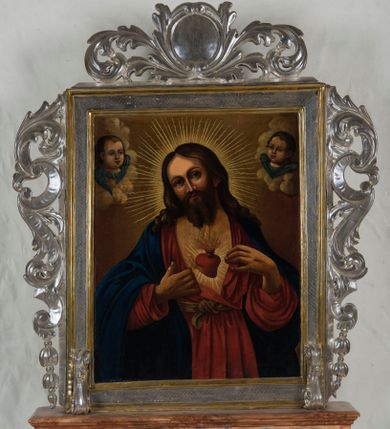 Zdjęcie nr 1: Feretron procesyjny tworzą dwa malowane na płótnie olejne obrazy ujęte w srebrzone ramy, których krawędzie wyznaczają profilowane i złocone listwy, ustawione na prostopadłościennym postumencie. Po bokach ram znajdują się ażurowe, srebrzone uszaki powstałe ze stylizowanych wici akantowych. Zwieńczenie feretronu utworzono z owalnego kartusza otoczonego ażurową, srebrzoną stylizowaną wicią akantową. Na awersie feretronu umieszczono przedstawienie Najświętszego Serca Pana Jezusa, a na rewersie św. Izydora. Postument został zaopatrzony w parę otworów do włożenia drążków umożliwiających noszenie feretronu. Podstawę i zwieńczenie postumentu dekoruje profilowana listwa, natomiast boki jasna brązowo-ochrowa marmoryzacja. Na awersie feretronu wyobrażono w trzech czwartych stojącego Chrystusa ukazującego swoje serce. Zbawiciel ma lekko pochyloną głowę w prawo, obiema zaś przebitymi dłońmi rozsuwa tunikę na piersi, odsłaniając przebite serce. Serce otaczają  złociste promienie. Z rany oraz u góry serca widać wydobywające się płomienie. Twarz Chrystusa jest pociągła. Otaczają ją długie brązowe włosy opadające puklami na ramiona oraz brązowa broda na dole nieznacznie rozdwojona. Twarz Zbawiciela charakteryzuje się wysokim czołem, długim, wąskim nosem i wydatnymi ustami. Chrystus szeroko otwartymi niebieskimi oczami wpatruje się w widza. Jego głowę otaczają złociste promienie. Ubrany jest w luźną, czerwoną tunikę przewiązaną w pasie jasnoochrową szarfą i narzucony na ramiona niebieski płaszcz, którego prawa poła przerzucona jest przez prawe przedramię. Zbawiciel został ukazany na jasnoochrowym tle. Po obu stronach jego głowy na jasnych obłokach widać dwie główki uskrzydlonych aniołków. Mają okrągłe głowy o pucołowatych policzkach z wydatnymi noskami i ustami. Unoszą się na niebieskich skrzydełkach. Na rewersie feretronu umieszczono przedstawienie św. Izydora. Święty został ukazany podczas modlitwy na pierwszym planie, klęcząc przed fragmentem bryły kościoła z półokrągłym oknem o mocno wyartykułowanym glifie. Górną część świątyni okrywają obłoki, z których wyłania się Madonna z Dzieciątkiem. Izydor ukazany został w całej postaci zwrócony w trzech czwartych w prawo z modlitewnie złożonymi rękami na wysokości piersi. O lewe przedramię ma oparty drewniany rydel u dołu okuty metalem. Jego głowa otoczona świetlistym nimbem jest lekko pochylona w prawo. Ma owalną twarz o wyrazistych rysach z dużym nosem i mięsistymi wargami oraz smutnie patrzącymi oczami. Otaczają ją krótkie brązowe włosy odsłaniające lewe ucho oraz krótki zarost. Ubrany jest w białą koszulę z aksamitką pod szyją, zapiętą zieloną kamizelkę oraz rozpięty niebieski surdut z rzędem złotych guzików i czerwone spodnie. Na nogach ma brązowe buty z wysokimi cholewami. Przy jego kolanach pod niewielkim drzewkiem leży brązowy kapelusz z szerokim rondem. W lewym rogu obrazu wyobrażono siedzącą na obłokach Madonnę, ukazaną w trzech czwartych w prawo. Przed sobą obiema rękami trzyma na kolanach Dzieciątko. Maria ma owalną twarz o jasnej karnacji z wydatnym nosem i ustami. Jej  głowę okoloną świetlistym nimbem otaczają długie brązowe włosy opadające na ramiona. Wokół wydekoltowanej szyi widać białą chustę skrzyżowaną na piersi. Madonna ubrana jest w czerwoną suknię przewiązaną w talii i niebieski płaszcz narzucony na ramiona, którego poły okrywają jej kolana. Mały Jezus przedstawiony jest w trzech czwartych w prawo. W lewej ręce trzyma błękitny glob, a prawą unosi w geście błogosławieństwa. Ma owalną twarz o jasnej karnacji z wydatnym nosem i ustami oraz wysokim czołem. Głowę okalają krótkie włosy i otacza świetlisty nimb. Zbawiciel ubrany jest w jasną tunikę odsłaniającą fragment stóp. Na drugim planie za modlącym się Izydorem wyobrażono dwa epizody z jego legendy. Z lewej strony pod ścianą kościoła widać Izydora nauczającego pięcioosobową grupę siedzących przed nim na ziemi ludzi. Święty obiema rękami trzyma książkę. Ubrany jest w kapelusz, białą koszulę, niebieski surdut, czerwone spodnie i buty z wysokimi cholewami. Dwóch ze słuchaczy siedzących z prawej strony ubranych jest w jasne szaty i zawoje na głowach. Natomiast trójka pozostałych to mężczyzna w kapeluszu z kosturem w lewej ręce odziany w łachmany, a także dwie postacie ukazane od tyłu ubrane w szaty z kapturami na głowach. Z tyłu z prawej strony Izydora widać anioła orzącego ziemię pługiem ciągnionym przez woła. Anioł z rozpostartymi skrzydłami w nieznacznym rozkroku ujęty został w trzech czwartych w lewo. Ubrany jest w tunikę sięgającą kolan z rozcięciem u dołu z przodu oraz sandały wiązane pod kolanami. Za nim w oddali widać klęczącego Izydora przed drewnianym krzyżem zatkniętym na skalnym wzgórku przy którym rosną trzy drzewa ułożone w szeregu. Tłem dla całego przedstawienia jest ciemne burzowe niebo rozjaśnione przy linii horyzontu. W lewym, dolnym rogu obrazu widać jasny napis „S(ANCTUS) ISIDORUS / AGRICOLA, HIS”.

