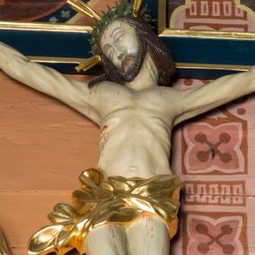 Zdjęcie nr 1: Na niebieskim, drewnianym krzyżu o ramionach wykończonych profilowanymi, złoconymi listwami zawieszono pełnoplastyczną rzeźbę ukrzyżowanego Chrystusa. Ponad jego głową przytwierdzono złocony titulus w formie krótkiej, wygiętej, podłużnej banderoli z inskrypcją &quot;IN / RI&quot;. Ukrzyżowany Chrystus o jasnej karnacji ciała ma ukośnie wyciągnięte, sztywne ręce  o przybitych do krzyża dłoniach oraz założoną nogę prawą na lewą, przytwierdzone jednym gwoździem. Jego ciało jest szczupłe. Ukrzyżowany ma zapadniętą klatkę piersiową, podkreślone żebra i obojczyk. Głowa Jezusa w zielonej koronie cierniowej opada na prawe ramię. Twarz otacza krótki brązowy zarost oraz długie brązowe włosy przykrywające kark i opadające na prawe ramię. Zbawiciel ma zamknięte oczy, prosty nos i wąskie usta. Na czole, szyi, ramionach, przy przebitym boku, dłoniach i stopach oraz na nogach widoczne są stróżki krwi. W partii bioder ciało Chrystusa okrywa przewiązane, złocone perizonium przechodzące w rozwiany feston przy prawym boku.