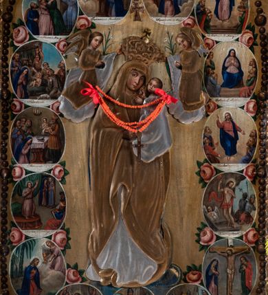 Zdjęcie nr 2: Feretron uzyskał kształt stojącego prostokąta zamkniętego łukiem odcinkowym, w który wprawiono dwustronnie malowany obraz ujęty w złocone pierwotnie ramy dekorowane ornamentem palmetowym. Ramy otacza ażurowa, płaskorzeźbiona i złocona stylizowana wić akantowa. Obramienie przymocowane jest do bladoniebieskiej podstawy w kształcie leżącego, profilowanego graniastosłupa przeprutego dwoma kwadratowymi otworami przeznaczonymi na zakładanie drążków procesyjnych z metalowymi uchwytami po bokach. Na awersie wyobrażono Matkę Boską Różańcową otoczoną owalnymi medalionami ilustrującymi tajemnice różańcowe. W centrum kompozycji ukazano stojącą postać Madonny z Dzieciątkiem z koronującymi ją dwoma aniołami. Maria ujęta została frontalnie z głową widoczną w trzech czwartych lekko pochyloną w prawo. Na lewym przedramieniu trzyma małego Jezusa, którego podtrzymuje prawą ręką. Matka Boska ma owalną twarz o jasnej karnacji, rumianych policzka, wydatnym nosie i ustach. Stoi na półksiężycu opartym o glob. Pod jej stopami widoczny jest deptany wąż. Trzymane przez nią Dzieciątko ujęte zostało w trzech czwartych w lewo. Jezus prawą rączką błogosławi a lewą wskazuje na matkę. Ma owalną twarz o jasnej karnacji z rumianymi policzkami, wydatnym nosem i ustami, okoloną krótkimi włosami. Zarówno postać Marii, jak i Dzieciątka okrywa złocona i srebrzona wotywna, tekturowa sukienka. Na głowę Marii dwóch aniołów widocznych po obu jej stronach nakłada koronę, osłoniętą złoconą koroną wotywną. Obie postaci okrywają srebrzone i złocone tekturowe sukienki wotywne odsłaniające tylko twarze o jasnej karnacji, wydatnym nosie i ustach, otoczone jasnobrązowymi włosami i trzymane w rękach lilie. Pod szyją Marii do sukienki przymocowano sznur korali z krzyżykiem. Wokół centralnych postaci w niewielkich, owalnych medalionach rozmieszczono przedstawienia ilustrujące piętnaście tajemnic różańcowych. Każda z nich oparta jest o kilkuosobową kompozycję, której towarzyszy podpis. Idąc od góry w lewo namalowano: Zwiastowanie Marii, Nawiedzenie św. Elżbiety, Boże Narodzenie, Ofiarowanie w świątyni, Znalezienie w świątyni, Modlitwa w Ogrójcu, Biczowanie, Cierniem ukoronowanie, Niesienie krzyża, Ukrzyżowanie, Zmartwychwstanie, Wniebowstąpienie, Zesłanie Ducha Świętego, Wniebowzięcie Marii, Ukoronowanie Marii w niebie. Narrację tajemnic rozdziela u góry wiszący na paciorkach różańca złocisty krzyżyk. Na rewersie przedstawiono Matkę Boską Niepokalanie Poczętą. W centrum kompozycji ukazano stojącą frontalnie na globie Madonnę depczącą węża. W odsuniętej od ciała prawej ręce trzyma lilię, lewą zaś przyciska do piersi. Maria ma owalną twarz o jasnej karnacji, rumiane policzki, szeroko otwarte oczy ze spojrzeniem skierowanym przed siebie, wydatny nos i usta. Jej głowę okalają jasnobrązowe włosy spływające na ramiona. Postać Madonny przykrywa tekturowa, złocona i srebrzona sukienka wotywna. Wokół zaś głowy widoczne są złocone promienie i gwiazdki. Madonnie przedstawionej na jasnoochrowych, rozjaśnionych obłokach towarzyszą cztery pary uskrzydlonych główek anielskich ustawionych po obu jej stronach. Po obu stronach globu główki są pojedyncze. Twarze aniołków mają jasne karnacje, pucułowate i rumiane policzki. Ich głowy otaczają krótkie, jasne włosy. 