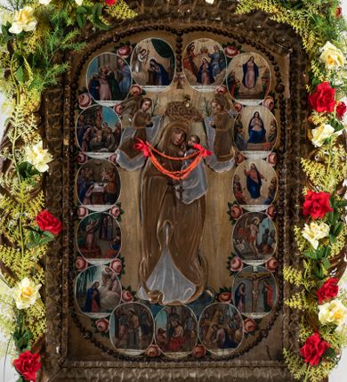 Zdjęcie nr 1: Feretron uzyskał kształt stojącego prostokąta zamkniętego łukiem odcinkowym, w który wprawiono dwustronnie malowany obraz ujęty w złocone pierwotnie ramy dekorowane ornamentem palmetowym. Ramy otacza ażurowa, płaskorzeźbiona i złocona stylizowana wić akantowa. Obramienie przymocowane jest do bladoniebieskiej podstawy w kształcie leżącego, profilowanego graniastosłupa przeprutego dwoma kwadratowymi otworami przeznaczonymi na zakładanie drążków procesyjnych z metalowymi uchwytami po bokach. Na awersie wyobrażono Matkę Boską Różańcową otoczoną owalnymi medalionami ilustrującymi tajemnice różańcowe. W centrum kompozycji ukazano stojącą postać Madonny z Dzieciątkiem z koronującymi ją dwoma aniołami. Maria ujęta została frontalnie z głową widoczną w trzech czwartych lekko pochyloną w prawo. Na lewym przedramieniu trzyma małego Jezusa, którego podtrzymuje prawą ręką. Matka Boska ma owalną twarz o jasnej karnacji, rumianych policzka, wydatnym nosie i ustach. Stoi na półksiężycu opartym o glob. Pod jej stopami widoczny jest deptany wąż. Trzymane przez nią Dzieciątko ujęte zostało w trzech czwartych w lewo. Jezus prawą rączką błogosławi a lewą wskazuje na matkę. Ma owalną twarz o jasnej karnacji z rumianymi policzkami, wydatnym nosem i ustami, okoloną krótkimi włosami. Zarówno postać Marii, jak i Dzieciątka okrywa złocona i srebrzona wotywna, tekturowa sukienka. Na głowę Marii dwóch aniołów widocznych po obu jej stronach nakłada koronę, osłoniętą złoconą koroną wotywną. Obie postaci okrywają srebrzone i złocone tekturowe sukienki wotywne odsłaniające tylko twarze o jasnej karnacji, wydatnym nosie i ustach, otoczone jasnobrązowymi włosami i trzymane w rękach lilie. Pod szyją Marii do sukienki przymocowano sznur korali z krzyżykiem. Wokół centralnych postaci w niewielkich, owalnych medalionach rozmieszczono przedstawienia ilustrujące piętnaście tajemnic różańcowych. Każda z nich oparta jest o kilkuosobową kompozycję, której towarzyszy podpis. Idąc od góry w lewo namalowano: Zwiastowanie Marii, Nawiedzenie św. Elżbiety, Boże Narodzenie, Ofiarowanie w świątyni, Znalezienie w świątyni, Modlitwa w Ogrójcu, Biczowanie, Cierniem ukoronowanie, Niesienie krzyża, Ukrzyżowanie, Zmartwychwstanie, Wniebowstąpienie, Zesłanie Ducha Świętego, Wniebowzięcie Marii, Ukoronowanie Marii w niebie. Narrację tajemnic rozdziela u góry wiszący na paciorkach różańca złocisty krzyżyk. Na rewersie przedstawiono Matkę Boską Niepokalanie Poczętą. W centrum kompozycji ukazano stojącą frontalnie na globie Madonnę depczącą węża. W odsuniętej od ciała prawej ręce trzyma lilię, lewą zaś przyciska do piersi. Maria ma owalną twarz o jasnej karnacji, rumiane policzki, szeroko otwarte oczy ze spojrzeniem skierowanym przed siebie, wydatny nos i usta. Jej głowę okalają jasnobrązowe włosy spływające na ramiona. Postać Madonny przykrywa tekturowa, złocona i srebrzona sukienka wotywna. Wokół zaś głowy widoczne są złocone promienie i gwiazdki. Madonnie przedstawionej na jasnoochrowych, rozjaśnionych obłokach towarzyszą cztery pary uskrzydlonych główek anielskich ustawionych po obu jej stronach. Po obu stronach globu główki są pojedyncze. Twarze aniołków mają jasne karnacje, pucułowate i rumiane policzki. Ich głowy otaczają krótkie, jasne włosy. 