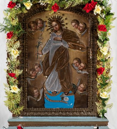 Zdjęcie nr 8: Feretron uzyskał kształt stojącego prostokąta zamkniętego łukiem odcinkowym, w który wprawiono dwustronnie malowany obraz ujęty w złocone pierwotnie ramy dekorowane ornamentem palmetowym. Ramy otacza ażurowa, płaskorzeźbiona i złocona stylizowana wić akantowa. Obramienie przymocowane jest do bladoniebieskiej podstawy w kształcie leżącego, profilowanego graniastosłupa przeprutego dwoma kwadratowymi otworami przeznaczonymi na zakładanie drążków procesyjnych z metalowymi uchwytami po bokach. Na awersie wyobrażono Matkę Boską Różańcową otoczoną owalnymi medalionami ilustrującymi tajemnice różańcowe. W centrum kompozycji ukazano stojącą postać Madonny z Dzieciątkiem z koronującymi ją dwoma aniołami. Maria ujęta została frontalnie z głową widoczną w trzech czwartych lekko pochyloną w prawo. Na lewym przedramieniu trzyma małego Jezusa, którego podtrzymuje prawą ręką. Matka Boska ma owalną twarz o jasnej karnacji, rumianych policzka, wydatnym nosie i ustach. Stoi na półksiężycu opartym o glob. Pod jej stopami widoczny jest deptany wąż. Trzymane przez nią Dzieciątko ujęte zostało w trzech czwartych w lewo. Jezus prawą rączką błogosławi a lewą wskazuje na matkę. Ma owalną twarz o jasnej karnacji z rumianymi policzkami, wydatnym nosem i ustami, okoloną krótkimi włosami. Zarówno postać Marii, jak i Dzieciątka okrywa złocona i srebrzona wotywna, tekturowa sukienka. Na głowę Marii dwóch aniołów widocznych po obu jej stronach nakłada koronę, osłoniętą złoconą koroną wotywną. Obie postaci okrywają srebrzone i złocone tekturowe sukienki wotywne odsłaniające tylko twarze o jasnej karnacji, wydatnym nosie i ustach, otoczone jasnobrązowymi włosami i trzymane w rękach lilie. Pod szyją Marii do sukienki przymocowano sznur korali z krzyżykiem. Wokół centralnych postaci w niewielkich, owalnych medalionach rozmieszczono przedstawienia ilustrujące piętnaście tajemnic różańcowych. Każda z nich oparta jest o kilkuosobową kompozycję, której towarzyszy podpis. Idąc od góry w lewo namalowano: Zwiastowanie Marii, Nawiedzenie św. Elżbiety, Boże Narodzenie, Ofiarowanie w świątyni, Znalezienie w świątyni, Modlitwa w Ogrójcu, Biczowanie, Cierniem ukoronowanie, Niesienie krzyża, Ukrzyżowanie, Zmartwychwstanie, Wniebowstąpienie, Zesłanie Ducha Świętego, Wniebowzięcie Marii, Ukoronowanie Marii w niebie. Narrację tajemnic rozdziela u góry wiszący na paciorkach różańca złocisty krzyżyk. Na rewersie przedstawiono Matkę Boską Niepokalanie Poczętą. W centrum kompozycji ukazano stojącą frontalnie na globie Madonnę depczącą węża. W odsuniętej od ciała prawej ręce trzyma lilię, lewą zaś przyciska do piersi. Maria ma owalną twarz o jasnej karnacji, rumiane policzki, szeroko otwarte oczy ze spojrzeniem skierowanym przed siebie, wydatny nos i usta. Jej głowę okalają jasnobrązowe włosy spływające na ramiona. Postać Madonny przykrywa tekturowa, złocona i srebrzona sukienka wotywna. Wokół zaś głowy widoczne są złocone promienie i gwiazdki. Madonnie przedstawionej na jasnoochrowych, rozjaśnionych obłokach towarzyszą cztery pary uskrzydlonych główek anielskich ustawionych po obu jej stronach. Po obu stronach globu główki są pojedyncze. Twarze aniołków mają jasne karnacje, pucułowate i rumiane policzki. Ich głowy otaczają krótkie, jasne włosy. 