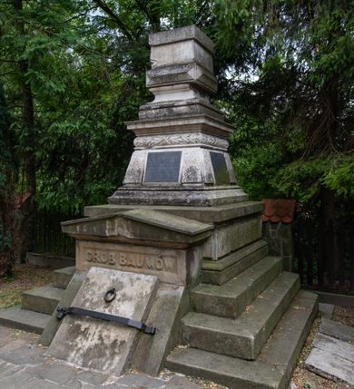 Zdjęcie nr 2: Nagrobek ustawiony na trójstopniowej podstawie i na cokole, w których na froncie mieści się wejście do grobu w formie przełamanego pod kątem leżącego prostokąta zamkniętego trójkątnym przyczółkiem z niszą, u spodu z reliefem: „GRÓB BAUMÓW”. Górna część nagrobka w kształcie dwustrefowego obelisku: dolna partia w formie ściętego ostrosłupa na profilowanym cokole, w polu trzech spośród czterech fakturowanych ścianek tablice, powyżej czworoboczny wałek dekorowany płaskorzeźbionymi gałązkami laurowymi przeplatanymi z wstęgą, strefa zakończona gzymsem. Górna część zwężająca się ku górze w postaci wklęsło-wypukłego profilowanego cokołu dźwigającego kostkę dekorowaną z czterech stron kaboszonami oraz sześcian. 
Płyta na południowej ściance bocznej: „ANTONI BARON BAUM / C(ESARSKO) K(RÓLEWSKI) RADCA DWORU / URODZONY 6 WRZEŚNIA 1763. / ZMARŁ 29 WRZEŚNIA 1829 R(OKU) / HELENA / BARONOWA BAUMOWA / ŻONA ANTONIEGO / *1797 + 1884.”. Płyta na ściance frontowej: „JÓZEF BARON BAUM / PREZES RADY POWIATOWEJ WADOWICKIEJ / POSEŁ NA SEJM KRAJOWY I DO RADY PAŃSTWA / WICE PREZES KOŁA POLSKIEGO W WIEDNIU / PREZES TOWARZYSTWA WZAJ(EMNYCH) UBEZP(IECZEŃ) W KRAKOWIE / I. T. D. / URODZONY 12. PAŹDŹ(IERNIKA) 1821 / ZMARŁ 11. MARCA 1883.” Płyta na północnej ściance bocznej: „WIKTOR JÓZEF B(A)R(ON) BAUM / URODZ(ONY) 23/10 1845 ZMARŁ 3/10 1846 / JÓZEFA B(A)R(ONOWA) BAUMÓWNA / URODZ(ONA) 4/4 1854 ZMARŁA 18/4 1854 R(OKU)”. Na cokole obelisku sygnatura: „E(DWARD) STEHLIK W KRAKOWIE”.