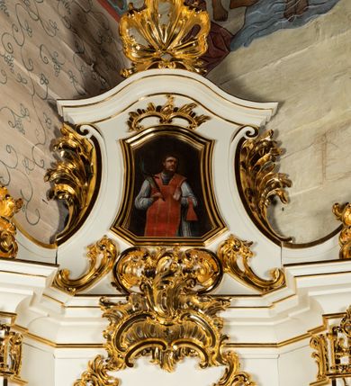 Zdjęcie nr 11: Ołtarz architektoniczny, jednokondygnacyjny, jednoosiowy ze zwieńczeniem. Ołtarz drewniany, sarkofagowy z drewnianą mensą. Retabulum ustawione na zdwojonym cokole o zryzalitowanych bokach. Kondygnacja ujęta jest  parą ustawionych ukośnie do wewnątrz, zdwojonych pilastrów z nałożoną w dolnej partii parą spływów wolutowych, wspierających przełamujący się ponad nimi, silnie wysunięty gzyms. Woluty spływów retabulum zdobione wydatnym rocaille&#039;m oraz parą rokokowych wazonów z gałązkami różyczek. Pole środkowe retabulum w kształcie stojącego prostokąta ujętego dołem odcinkowym łukiem nadwieszonym, od góry zamknięte łukiem wklęsło-wypukłym z uskokami; w polu obraz Matki Nieustającej Pomocy. Trzony pilastrów zdobione podwieszonymi gałązkami z różyczkami, a kapitele ornamentem rocaille&#039;owym. Górną partię środkowego pola retabulum ozdabia ornament rocaille&#039;owy. Zwieńczenie ujęte jest spływami wolutowymi o skośnie ustawionych dolnych partiach, zamknięte odcinkiem gzymsu w kształcie łuku wklęsło-wypukłego. Szczyt zwieńczenia w formie ażurowej, rocaille&#039;owej konchy. Pole środkowe o wklęsłych bokach, ściętych dolnych narożach, zamknięte łukiem wklęsło-wypukłym, ujęte profilowaną złoconą ramą; w środku obraz św. Walentego. Krawędzie spływów wolutowych zdobione parą gałązek palmowych. Struktura polichromowana na biało, cokół w kolorze jasnoszarym z żółtym profilowaniem; partie detalu architektonicznego i ornamentyki złocone i srebrzone.      

