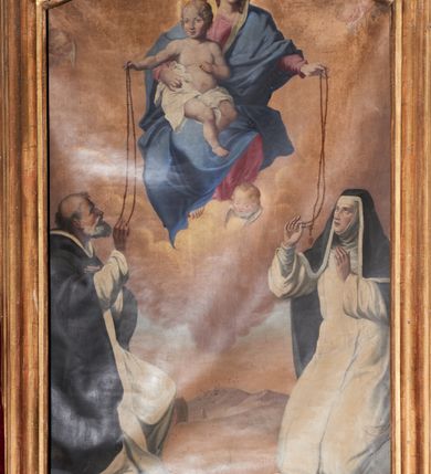 Zdjęcie nr 2: Obraz Matki Boskiej Różańcowej ze świętymi dominikańskimi w kształcie stojącego prostokąta, zamkniętego łukiem wklęsło-wypukłym z uskokami. Kompozycja dwustrefowa, w partii wyższej ukazana jest Matka Boska w pozycji siedzącej na obłokach, frontalnie, z Dzieciątkiem Jezus na prawym boku, lewą ręką podająca różaniec św. Katarzynie. Twarz o delikatnych rysach, oczy przymknięte, wzrok skierowany na św. Katarzynę; jasne i długie włosy. Maria ubrana jest w jasnoróżową suknię z długimi rękawami; błękitny płaszcz otulający całą postać oraz biały welon na głowie. Dzieciątko zwrócone jest trzy czwarte w lewo, ze skrzyżowanymi nogami, prawą ręką podaje różaniec św. Dominikowi, a lewą ma ugiętą w łokciu. Twarz pełna, zarumieniona, włosy jasne i kędzierzawe. Dzieciątko ubrane jest w białą pieluszkę, osłaniającą biodra. Matka Boska i Dzieciątko mają wokół głów koliste nimby, a na głowach zamknięte korony. W dolnej strefie, po lewej stronie obrazu klęczy św. Dominik, zwrócony w lewo, prawą ręką odbierający różaniec od Dzieciątka, a lewą ma złożoną na piersi. Twarz ukazana jest z lewego profilu o rysach twarzy starszego mężczyzny z siwą i krótką brodą, długim nosem, łysiną na głowie i śniadą cerą. Ubrany jest w płaszcz i habit dominikański. Poniżej widoczny jest niebieski glob ziemski oraz głowa psa z pochodnią w pysku. Po prawej stronie klęczy św. Katarzyna ze Sieny, zwrócona trzy czwarte w prawo, która prawą ręką odbiera różaniec od Marii, a lewą unosi ku górze. Twarz owalna z pełnymi ustami, krótkim nosem i dużymi oczami ze wzorkiem skierowanym na Matkę Boską. Ubrana jest w strój dominikański: habit, płaszcz i welon z podwiką. W oddali widoczny jest pejzaż górski i zabudowania. W górnej części kompozycji pochmurne niebo oraz uskrzydlone główki anielskie w narożach oraz jedna przy stopie Matki Boskiej. 
