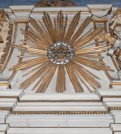 Zdjęcie nr 14: Ołtarz architektoniczny, jednokondygnacyjny, jednoosiowy ze zwieńczeniem. Mensa drewniana, sarkofagowa, ustawiona na parze nóżek w kształcie kul ujętych w górnej partii liśćmi laurowymi z kamiennym portatylem. Na ściance przedniej ozdobiona jest parą płycin w kształcie leżących prostokątów o wklęsłych bokach wewnętrznych; pomiędzy nimi płycina w kształcie koła ze złoconym napisem na niebieskim tle „ALTARE PRIVIL(EGIATUM)”. Retabulum ustawione jest na zdwojonym cokole o zryzalitowanych bokach. Nastawa ujęta parą zdwojonych pilastrów z kapitelami jońskimi, wspierających przełamujące się ponad nimi belkowanie. Pole środkowe retabulum w kształcie stojącego prostokąta, ujęte profilowaną i złoconą ramą z motywem wąskiej szarfy oplatającej cieniutki wałek; w polu obraz Najświętszego Serca Jezusa. Retabulum flankowane jest po bokach parą ażurowych uszaków w formie stylizowanej wici roślinnej z kwiatami. Górną partię trzonów pilastrów zdobi para festonów z liści laurowych, trzony dekorowane są grawerowanymi zwisami w formie gałązek z kwiatami i owocami. W dolnej i górnej partii pola środkowego retabulum ornamentyka rocaille’owa. Gzyms retabulum ozdabia jońska kostka. Zwieńczenie o wklęsłych bokach, ujęte parą wygiętych pilastrów na niewysokich cokołach, podtrzymujących wyłamujące się ponad nimi belkowanie. W polu głównym znajduje się promienista gloria z monogramem maryjnym pośrodku, otoczonym wieńcem z obłoków. Krawędzie boków zdobione są liściastymi gałązkami. Na gzymsie retabulum, po bokach ustawiona jest para aniołków. Struktura ołtarza polichromowana jest w odcieniach szarości, część dolna w kolorze ciemnoszarym, a górna w jasnoszarym; pola płycin antepedium malowane w odcieniach błękitów. Partie detalu architektonicznego i ornamentyka złocone i srebrzone. 
