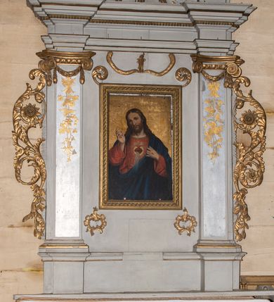 Zdjęcie nr 12: Ołtarz architektoniczny, jednokondygnacyjny, jednoosiowy ze zwieńczeniem. Mensa drewniana, sarkofagowa, ustawiona na parze nóżek w kształcie kul ujętych w górnej partii liśćmi laurowymi z kamiennym portatylem. Na ściance przedniej ozdobiona jest parą płycin w kształcie leżących prostokątów o wklęsłych bokach wewnętrznych; pomiędzy nimi płycina w kształcie koła ze złoconym napisem na niebieskim tle „ALTARE PRIVIL(EGIATUM)”. Retabulum ustawione jest na zdwojonym cokole o zryzalitowanych bokach. Nastawa ujęta parą zdwojonych pilastrów z kapitelami jońskimi, wspierających przełamujące się ponad nimi belkowanie. Pole środkowe retabulum w kształcie stojącego prostokąta, ujęte profilowaną i złoconą ramą z motywem wąskiej szarfy oplatającej cieniutki wałek; w polu obraz Najświętszego Serca Jezusa. Retabulum flankowane jest po bokach parą ażurowych uszaków w formie stylizowanej wici roślinnej z kwiatami. Górną partię trzonów pilastrów zdobi para festonów z liści laurowych, trzony dekorowane są grawerowanymi zwisami w formie gałązek z kwiatami i owocami. W dolnej i górnej partii pola środkowego retabulum ornamentyka rocaille’owa. Gzyms retabulum ozdabia jońska kostka. Zwieńczenie o wklęsłych bokach, ujęte parą wygiętych pilastrów na niewysokich cokołach, podtrzymujących wyłamujące się ponad nimi belkowanie. W polu głównym znajduje się promienista gloria z monogramem maryjnym pośrodku, otoczonym wieńcem z obłoków. Krawędzie boków zdobione są liściastymi gałązkami. Na gzymsie retabulum, po bokach ustawiona jest para aniołków. Struktura ołtarza polichromowana jest w odcieniach szarości, część dolna w kolorze ciemnoszarym, a górna w jasnoszarym; pola płycin antepedium malowane w odcieniach błękitów. Partie detalu architektonicznego i ornamentyka złocone i srebrzone. 
