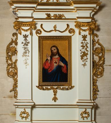 Zdjęcie nr 2: Ołtarz architektoniczny, jednokondygnacyjny, jednoosiowy ze zwieńczeniem. Mensa drewniana, sarkofagowa, ustawiona na parze nóżek w kształcie kul ujętych w górnej partii liśćmi laurowymi z kamiennym portatylem. Na ściance przedniej ozdobiona jest parą płycin w kształcie leżących prostokątów o wklęsłych bokach wewnętrznych; pomiędzy nimi płycina w kształcie koła ze złoconym napisem na niebieskim tle „ALTARE PRIVIL(EGIATUM)”. Retabulum ustawione jest na zdwojonym cokole o zryzalitowanych bokach. Nastawa ujęta parą zdwojonych pilastrów z kapitelami jońskimi, wspierających przełamujące się ponad nimi belkowanie. Pole środkowe retabulum w kształcie stojącego prostokąta, ujęte profilowaną i złoconą ramą z motywem wąskiej szarfy oplatającej cieniutki wałek; w polu obraz Najświętszego Serca Jezusa. Retabulum flankowane jest po bokach parą ażurowych uszaków w formie stylizowanej wici roślinnej z kwiatami. Górną partię trzonów pilastrów zdobi para festonów z liści laurowych, trzony dekorowane są grawerowanymi zwisami w formie gałązek z kwiatami i owocami. W dolnej i górnej partii pola środkowego retabulum ornamentyka rocaille’owa. Gzyms retabulum ozdabia jońska kostka. Zwieńczenie o wklęsłych bokach, ujęte parą wygiętych pilastrów na niewysokich cokołach, podtrzymujących wyłamujące się ponad nimi belkowanie. W polu głównym znajduje się promienista gloria z monogramem maryjnym pośrodku, otoczonym wieńcem z obłoków. Krawędzie boków zdobione są liściastymi gałązkami. Na gzymsie retabulum, po bokach ustawiona jest para aniołków. Struktura ołtarza polichromowana jest w odcieniach szarości, część dolna w kolorze ciemnoszarym, a górna w jasnoszarym; pola płycin antepedium malowane w odcieniach błękitów. Partie detalu architektonicznego i ornamentyka złocone i srebrzone. 
