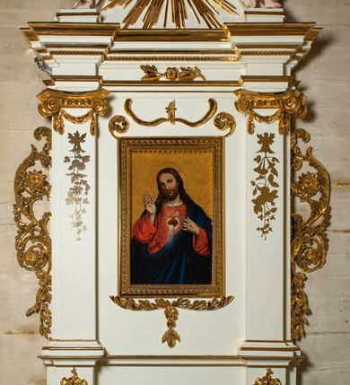 Zdjęcie nr 13: Ołtarz architektoniczny, jednokondygnacyjny, jednoosiowy ze zwieńczeniem. Mensa drewniana, sarkofagowa, ustawiona na parze nóżek w kształcie kul ujętych w górnej partii liśćmi laurowymi z kamiennym portatylem. Na ściance przedniej ozdobiona jest parą płycin w kształcie leżących prostokątów o wklęsłych bokach wewnętrznych; pomiędzy nimi płycina w kształcie koła ze złoconym napisem na niebieskim tle „ALTARE PRIVIL(EGIATUM)”. Retabulum ustawione jest na zdwojonym cokole o zryzalitowanych bokach. Nastawa ujęta parą zdwojonych pilastrów z kapitelami jońskimi, wspierających przełamujące się ponad nimi belkowanie. Pole środkowe retabulum w kształcie stojącego prostokąta, ujęte profilowaną i złoconą ramą z motywem wąskiej szarfy oplatającej cieniutki wałek; w polu obraz Najświętszego Serca Jezusa. Retabulum flankowane jest po bokach parą ażurowych uszaków w formie stylizowanej wici roślinnej z kwiatami. Górną partię trzonów pilastrów zdobi para festonów z liści laurowych, trzony dekorowane są grawerowanymi zwisami w formie gałązek z kwiatami i owocami. W dolnej i górnej partii pola środkowego retabulum ornamentyka rocaille’owa. Gzyms retabulum ozdabia jońska kostka. Zwieńczenie o wklęsłych bokach, ujęte parą wygiętych pilastrów na niewysokich cokołach, podtrzymujących wyłamujące się ponad nimi belkowanie. W polu głównym znajduje się promienista gloria z monogramem maryjnym pośrodku, otoczonym wieńcem z obłoków. Krawędzie boków zdobione są liściastymi gałązkami. Na gzymsie retabulum, po bokach ustawiona jest para aniołków. Struktura ołtarza polichromowana jest w odcieniach szarości, część dolna w kolorze ciemnoszarym, a górna w jasnoszarym; pola płycin antepedium malowane w odcieniach błękitów. Partie detalu architektonicznego i ornamentyka złocone i srebrzone. 
