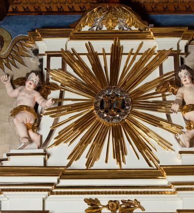 Zdjęcie nr 5: Ołtarz architektoniczny, jednokondygnacyjny, jednoosiowy ze zwieńczeniem. Mensa drewniana, sarkofagowa, ustawiona na parze nóżek w kształcie kul ujętych w górnej partii liśćmi laurowymi z kamiennym portatylem. Na ściance przedniej ozdobiona jest parą płycin w kształcie leżących prostokątów o wklęsłych bokach wewnętrznych; pomiędzy nimi płycina w kształcie koła ze złoconym napisem na niebieskim tle „ALTARE PRIVIL(EGIATUM)”. Retabulum ustawione jest na zdwojonym cokole o zryzalitowanych bokach. Nastawa ujęta parą zdwojonych pilastrów z kapitelami jońskimi, wspierających przełamujące się ponad nimi belkowanie. Pole środkowe retabulum w kształcie stojącego prostokąta, ujęte profilowaną i złoconą ramą z motywem wąskiej szarfy oplatającej cieniutki wałek; w polu obraz Najświętszego Serca Jezusa. Retabulum flankowane jest po bokach parą ażurowych uszaków w formie stylizowanej wici roślinnej z kwiatami. Górną partię trzonów pilastrów zdobi para festonów z liści laurowych, trzony dekorowane są grawerowanymi zwisami w formie gałązek z kwiatami i owocami. W dolnej i górnej partii pola środkowego retabulum ornamentyka rocaille’owa. Gzyms retabulum ozdabia jońska kostka. Zwieńczenie o wklęsłych bokach, ujęte parą wygiętych pilastrów na niewysokich cokołach, podtrzymujących wyłamujące się ponad nimi belkowanie. W polu głównym znajduje się promienista gloria z monogramem maryjnym pośrodku, otoczonym wieńcem z obłoków. Krawędzie boków zdobione są liściastymi gałązkami. Na gzymsie retabulum, po bokach ustawiona jest para aniołków. Struktura ołtarza polichromowana jest w odcieniach szarości, część dolna w kolorze ciemnoszarym, a górna w jasnoszarym; pola płycin antepedium malowane w odcieniach błękitów. Partie detalu architektonicznego i ornamentyka złocone i srebrzone. 
