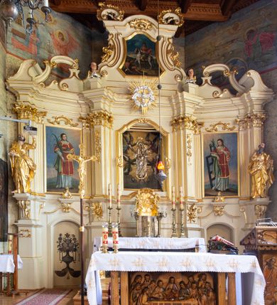 Zdjęcie nr 26: Nastawa ołtarzowa architektoniczna, trójosiowa, jednokondygnacyjna ze zwieńczeniem i bramkami. Ołtarz drewniany, prostopadłościenny; antepedium haftowane. Tabernakulum metalowe, fakturowane, w formie zbliżonej do prostopadłościennej skrzynki, ustawione na niskim cokole, o wypukłej ściance frontowej, flankowane parą kolumn o kompozytowych kapitelach. Drzwiczki w kształcie stojącego prostokąta, zamkniętego łukiem nadwieszonym; w polu kielich z hostią, a po bokach winna winorośl i kłosy zbóż. Powyżej jest tron wystawienia o fantazyjnym kształcie, ujęty po bokach wolutami, na których usadzone są dwa putta. W polu maska lunarna, otoczona promienistą glorią, a w zwieńczeniu muszla palmetowa. Nastawa ustawiona jest na wysokim, zdwojonym cokole, flankowana dwiema parami zdwojonych pilastrów, ustawionych ukośnie. Bramki w kształcie stojących prostokątów, zamkniętych półkoliście, w profilowanej obudowie zwieńczonej wolutowo. Drzwiczki dekorowane są malowanym bukietem kwiatów w wazonie. Kondygnacja o delikatnie wklęsłym przebiegu, ujęta dwiema parami zdwojonych, kanelowanych pilastrów, z których wewnętrzne ustawione są pod kątem. Podpory dźwigają pełne belkowanie, wyłamane nad osiami. Na linii wewnętrznych podpór ustawione są dwa cokoły, na których osadzono dwie główki aniołków, a na linii skrajnych podpór wolutowe przyczółki; z kolei pomiędzy nimi znajdują się fantazyjne woluty. W polu środkowym w ramie o kształcie stojącego prostokąta, zamkniętego łukiem wklęsło-wypukłym z uskokami umieszczony jest obraz Wniebowzięcia Najświętszej Marii Panny, a na zasuwie obraz św. Marcina oraz płótno przedstawiające Chrystusa Ukrzyżowanego. W osiach bocznych obrazy: po lewej św. Szczepan, a po prawej św. Wawrzyniec. Przed skrajnymi podporami ustawione są figury: po lewej św. Piotra, a po prawej św. Pawła. Nad polem głównym zawieszona jest gołębica Ducha Świętego na tle srebrzonych obłoków i promienistej glorii. Zwieńczenie w formie zbliżonej do leżącego prostokąta ujętego spływami wolutowymi, zamknięte profilowanym gzymsem i rocaille’ami. W polu obraz św. Marcina. Struktura polichromowana w kolorze jasnobeżowym, ornamentyka złocona, detale srebrzone.



