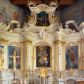 Zdjęcie nr 1: Nastawa ołtarzowa architektoniczna, trójosiowa, jednokondygnacyjna ze zwieńczeniem i bramkami. Ołtarz drewniany, prostopadłościenny; antepedium haftowane. Tabernakulum metalowe, fakturowane, w formie zbliżonej do prostopadłościennej skrzynki, ustawione na niskim cokole, o wypukłej ściance frontowej, flankowane parą kolumn o kompozytowych kapitelach. Drzwiczki w kształcie stojącego prostokąta, zamkniętego łukiem nadwieszonym; w polu kielich z hostią, a po bokach winna winorośl i kłosy zbóż. Powyżej jest tron wystawienia o fantazyjnym kształcie, ujęty po bokach wolutami, na których usadzone są dwa putta. W polu maska lunarna, otoczona promienistą glorią, a w zwieńczeniu muszla palmetowa. Nastawa ustawiona jest na wysokim, zdwojonym cokole, flankowana dwiema parami zdwojonych pilastrów, ustawionych ukośnie. Bramki w kształcie stojących prostokątów, zamkniętych półkoliście, w profilowanej obudowie zwieńczonej wolutowo. Drzwiczki dekorowane są malowanym bukietem kwiatów w wazonie. Kondygnacja o delikatnie wklęsłym przebiegu, ujęta dwiema parami zdwojonych, kanelowanych pilastrów, z których wewnętrzne ustawione są pod kątem. Podpory dźwigają pełne belkowanie, wyłamane nad osiami. Na linii wewnętrznych podpór ustawione są dwa cokoły, na których osadzono dwie główki aniołków, a na linii skrajnych podpór wolutowe przyczółki; z kolei pomiędzy nimi znajdują się fantazyjne woluty. W polu środkowym w ramie o kształcie stojącego prostokąta, zamkniętego łukiem wklęsło-wypukłym z uskokami umieszczony jest obraz Wniebowzięcia Najświętszej Marii Panny, a na zasuwie obraz św. Marcina oraz płótno przedstawiające Chrystusa Ukrzyżowanego. W osiach bocznych obrazy: po lewej św. Szczepan, a po prawej św. Wawrzyniec. Przed skrajnymi podporami ustawione są figury: po lewej św. Piotra, a po prawej św. Pawła. Nad polem głównym zawieszona jest gołębica Ducha Świętego na tle srebrzonych obłoków i promienistej glorii. Zwieńczenie w formie zbliżonej do leżącego prostokąta ujętego spływami wolutowymi, zamknięte profilowanym gzymsem i rocaille’ami. W polu obraz św. Marcina. Struktura polichromowana w kolorze jasnobeżowym, ornamentyka złocona, detale srebrzone.



