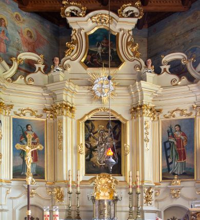 Zdjęcie nr 1: Nastawa ołtarzowa architektoniczna, trójosiowa, jednokondygnacyjna ze zwieńczeniem i bramkami. Ołtarz drewniany, prostopadłościenny; antepedium haftowane. Tabernakulum metalowe, fakturowane, w formie zbliżonej do prostopadłościennej skrzynki, ustawione na niskim cokole, o wypukłej ściance frontowej, flankowane parą kolumn o kompozytowych kapitelach. Drzwiczki w kształcie stojącego prostokąta, zamkniętego łukiem nadwieszonym; w polu kielich z hostią, a po bokach winna winorośl i kłosy zbóż. Powyżej jest tron wystawienia o fantazyjnym kształcie, ujęty po bokach wolutami, na których usadzone są dwa putta. W polu maska lunarna, otoczona promienistą glorią, a w zwieńczeniu muszla palmetowa. Nastawa ustawiona jest na wysokim, zdwojonym cokole, flankowana dwiema parami zdwojonych pilastrów, ustawionych ukośnie. Bramki w kształcie stojących prostokątów, zamkniętych półkoliście, w profilowanej obudowie zwieńczonej wolutowo. Drzwiczki dekorowane są malowanym bukietem kwiatów w wazonie. Kondygnacja o delikatnie wklęsłym przebiegu, ujęta dwiema parami zdwojonych, kanelowanych pilastrów, z których wewnętrzne ustawione są pod kątem. Podpory dźwigają pełne belkowanie, wyłamane nad osiami. Na linii wewnętrznych podpór ustawione są dwa cokoły, na których osadzono dwie główki aniołków, a na linii skrajnych podpór wolutowe przyczółki; z kolei pomiędzy nimi znajdują się fantazyjne woluty. W polu środkowym w ramie o kształcie stojącego prostokąta, zamkniętego łukiem wklęsło-wypukłym z uskokami umieszczony jest obraz Wniebowzięcia Najświętszej Marii Panny, a na zasuwie obraz św. Marcina oraz płótno przedstawiające Chrystusa Ukrzyżowanego. W osiach bocznych obrazy: po lewej św. Szczepan, a po prawej św. Wawrzyniec. Przed skrajnymi podporami ustawione są figury: po lewej św. Piotra, a po prawej św. Pawła. Nad polem głównym zawieszona jest gołębica Ducha Świętego na tle srebrzonych obłoków i promienistej glorii. Zwieńczenie w formie zbliżonej do leżącego prostokąta ujętego spływami wolutowymi, zamknięte profilowanym gzymsem i rocaille’ami. W polu obraz św. Marcina. Struktura polichromowana w kolorze jasnobeżowym, ornamentyka złocona, detale srebrzone.



