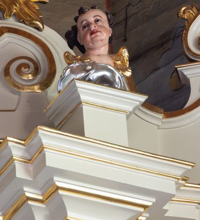 Zdjęcie nr 8: Nastawa ołtarzowa architektoniczna, trójosiowa, jednokondygnacyjna ze zwieńczeniem i bramkami. Ołtarz drewniany, prostopadłościenny; antepedium haftowane. Tabernakulum metalowe, fakturowane, w formie zbliżonej do prostopadłościennej skrzynki, ustawione na niskim cokole, o wypukłej ściance frontowej, flankowane parą kolumn o kompozytowych kapitelach. Drzwiczki w kształcie stojącego prostokąta, zamkniętego łukiem nadwieszonym; w polu kielich z hostią, a po bokach winna winorośl i kłosy zbóż. Powyżej jest tron wystawienia o fantazyjnym kształcie, ujęty po bokach wolutami, na których usadzone są dwa putta. W polu maska lunarna, otoczona promienistą glorią, a w zwieńczeniu muszla palmetowa. Nastawa ustawiona jest na wysokim, zdwojonym cokole, flankowana dwiema parami zdwojonych pilastrów, ustawionych ukośnie. Bramki w kształcie stojących prostokątów, zamkniętych półkoliście, w profilowanej obudowie zwieńczonej wolutowo. Drzwiczki dekorowane są malowanym bukietem kwiatów w wazonie. Kondygnacja o delikatnie wklęsłym przebiegu, ujęta dwiema parami zdwojonych, kanelowanych pilastrów, z których wewnętrzne ustawione są pod kątem. Podpory dźwigają pełne belkowanie, wyłamane nad osiami. Na linii wewnętrznych podpór ustawione są dwa cokoły, na których osadzono dwie główki aniołków, a na linii skrajnych podpór wolutowe przyczółki; z kolei pomiędzy nimi znajdują się fantazyjne woluty. W polu środkowym w ramie o kształcie stojącego prostokąta, zamkniętego łukiem wklęsło-wypukłym z uskokami umieszczony jest obraz Wniebowzięcia Najświętszej Marii Panny, a na zasuwie obraz św. Marcina oraz płótno przedstawiające Chrystusa Ukrzyżowanego. W osiach bocznych obrazy: po lewej św. Szczepan, a po prawej św. Wawrzyniec. Przed skrajnymi podporami ustawione są figury: po lewej św. Piotra, a po prawej św. Pawła. Nad polem głównym zawieszona jest gołębica Ducha Świętego na tle srebrzonych obłoków i promienistej glorii. Zwieńczenie w formie zbliżonej do leżącego prostokąta ujętego spływami wolutowymi, zamknięte profilowanym gzymsem i rocaille’ami. W polu obraz św. Marcina. Struktura polichromowana w kolorze jasnobeżowym, ornamentyka złocona, detale srebrzone.



