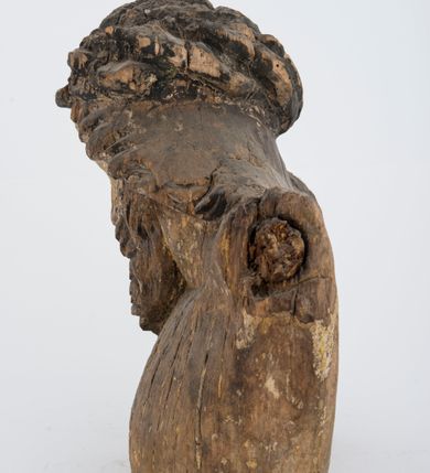 Zdjęcie nr 8: Fragment pełnoplastycznej rzeźby Jezusa Ukrzyżowanego.  Zachował się tors wraz z głową pochyloną na prawy bark. Twarz pociągła z wąskim, prostym nosem, zamkniętymi oczami, wąskimi, lekko rozchylonymi ustami, okolona zarostem i długimi, zwiniętymi w pukle włosami opadającymi na prawe ramię i plecy; na głowie korona cierniowa. 