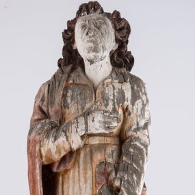 Zdjęcie nr 1: Pełnoplastyczna rzeźba św. Jana Ewangelisty stojącego w kontrapoście, z lewą noga ugiętą w kolanie. Święty jest ukazany frontalnie, prawą rękę składa na piersi, w lewej, opuszczonej wzdłuż ciała trzyma zamkniętą księgę. Głowa odchylona do tyłu, twarz podłużna, z prostym nosem, wąskimi ustami, wydatnym podbródkiem, okolona brązowymi włosami, które opadają na ramiona i plecy. Jan jest ubrany w żółtą, rozciętą pod szyją suknię przepasaną w talii oraz czerwony płaszcz zarzucony na prawe ramię i owijający się wokół lewego biodra, opadający prostymi fałdami w dół. Spod tuniki widoczne bose stopy. 