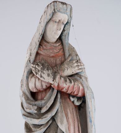 Zdjęcie nr 1: Pełnoplastyczna rzeźba Matki Boskiej Bolesnej ustawionej frontalnie, w lekkim kontrapoście, z prawą nogą ugiętą w kolanie i rękami skrzyżowanymi na piersi. Maria skręca głowę nieznacznie w lewo, spogląda smutno w dół. Na podłużnej twarzy odznaczają się wysokie czoło, duże, migdałowe, półprzymknięte oczy, wąski nos, niewielkie usta oraz szeroki podbródek. Ubrana jest w czerwoną suknię o wąskich, marszczących się równoległymi fałdami rękawach i kołnierzu, spływającą do ziemi podłużnymi fałdami. Na nią nałożony ma jasnoniebieski, zarzucony na głowę płaszcz, który zakrywa plecy i spływa na ramiona. Prawa poła przytrzymana między rękami zawija się przy prawym biodrze łamanymi fałdami. Spod sukni widoczne ciemnobrązowe, szpiczaste buty.