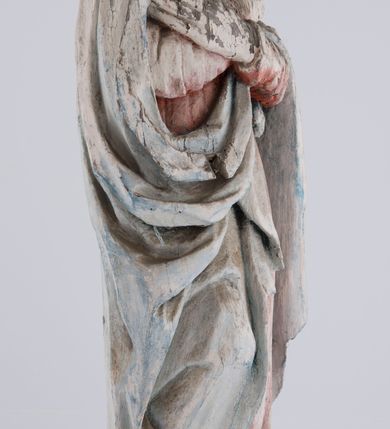 Zdjęcie nr 3: Pełnoplastyczna rzeźba Matki Boskiej Bolesnej ustawionej frontalnie, w lekkim kontrapoście, z prawą nogą ugiętą w kolanie i rękami skrzyżowanymi na piersi. Maria skręca głowę nieznacznie w lewo, spogląda smutno w dół. Na podłużnej twarzy odznaczają się wysokie czoło, duże, migdałowe, półprzymknięte oczy, wąski nos, niewielkie usta oraz szeroki podbródek. Ubrana jest w czerwoną suknię o wąskich, marszczących się równoległymi fałdami rękawach i kołnierzu, spływającą do ziemi podłużnymi fałdami. Na nią nałożony ma jasnoniebieski, zarzucony na głowę płaszcz, który zakrywa plecy i spływa na ramiona. Prawa poła przytrzymana między rękami zawija się przy prawym biodrze łamanymi fałdami. Spod sukni widoczne ciemnobrązowe, szpiczaste buty.