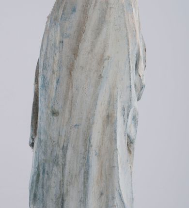 Zdjęcie nr 6: Pełnoplastyczna rzeźba Matki Boskiej Bolesnej ustawionej frontalnie, w lekkim kontrapoście, z prawą nogą ugiętą w kolanie i rękami skrzyżowanymi na piersi. Maria skręca głowę nieznacznie w lewo, spogląda smutno w dół. Na podłużnej twarzy odznaczają się wysokie czoło, duże, migdałowe, półprzymknięte oczy, wąski nos, niewielkie usta oraz szeroki podbródek. Ubrana jest w czerwoną suknię o wąskich, marszczących się równoległymi fałdami rękawach i kołnierzu, spływającą do ziemi podłużnymi fałdami. Na nią nałożony ma jasnoniebieski, zarzucony na głowę płaszcz, który zakrywa plecy i spływa na ramiona. Prawa poła przytrzymana między rękami zawija się przy prawym biodrze łamanymi fałdami. Spod sukni widoczne ciemnobrązowe, szpiczaste buty.