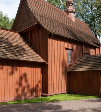 Zdjęcie nr 30: Kościół usytuowany na wzniesieniu, w otoczeniu bogatego drzewostanu. Orientowany, jednonawowy, z zamkniętym trójbocznie prezbiterium i przylegającą od północy zakrystią. Od południa i zachodu do korpusu przylegają kruchty. Nawa na planie prostokąta, szersza od prezbiterium. Wewnątrz pozorne sklepienie kolebkowe, w nawie z płaskimi odcinkami stropowymi po bokach, podpartymi na profilowanych słupach ustawionych na cokołach. Ściany opięte pilastrami naśladującymi formę słupów. Prezbiterium od korpusu oddziela łuk tęczowy, półkolisty, profilowany, ozdobiony ornamentem sznurowym, wsparty na profilowanych kroksztynach dekorowanych drewnianymi rozetami. Od zachodu parapet chóru muzycznego na planie prostokąta oparty na dwóch wielobocznych słupach, front dekorowany motywem w formie powtarzających się zwróconych do siebie par esownic i napisem „MIŁOŚCIĄ WIECZNĄ UMIŁOWAŁEM CIĘ” rozdzielonym wizerunkiem pelikana karmiącego młode własną krwią. Od południa schody prowadzące na chór z analogiczną dekoracją. Fasada prosta, zamknięta daszkiem krytym gontem, zwieńczona trójkątnie. Korpus z trzech stron wzmocniony belkami. Od strony północnej i południowej po dwa okna prostokątne zwieńczone niewielkimi blaszanymi daszkami. Prezbiterium od strony południowej opięte dwoma belkami, z prostokątnym oknem. Na ścianie wschodniej, na zewnątrz, kapliczka z ceramicznym przedstawieniem Matki Boskiej z Dzieciątkiem. W ścianach wschodniej i północnej zakrystii po jednym prostokątnym oknie. Dach dwuspadowy, o jednej kalenicy, od wschodu odzwierciedla układ ścian prezbiterium. Kruchty przykryte dachami dwuspadowymi. Dachy kryte gontem. Na przecięciu korpusu z prezbiterium blaszana, ośmioboczna wieżyczka na sygnaturkę zwieńczona hełmem baniastym ze spłaszczoną kulą z krzyżem. 