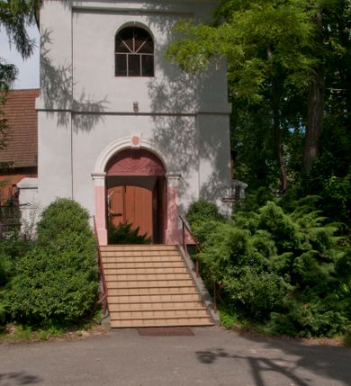 Zdjęcie nr 16: Kościół usytuowany na wzniesieniu, w otoczeniu bogatego drzewostanu. Orientowany, jednonawowy, z zamkniętym trójbocznie prezbiterium i przylegającą od północy zakrystią. Od południa i zachodu do korpusu przylegają kruchty. Nawa na planie prostokąta, szersza od prezbiterium. Wewnątrz pozorne sklepienie kolebkowe, w nawie z płaskimi odcinkami stropowymi po bokach, podpartymi na profilowanych słupach ustawionych na cokołach. Ściany opięte pilastrami naśladującymi formę słupów. Prezbiterium od korpusu oddziela łuk tęczowy, półkolisty, profilowany, ozdobiony ornamentem sznurowym, wsparty na profilowanych kroksztynach dekorowanych drewnianymi rozetami. Od zachodu parapet chóru muzycznego na planie prostokąta oparty na dwóch wielobocznych słupach, front dekorowany motywem w formie powtarzających się zwróconych do siebie par esownic i napisem „MIŁOŚCIĄ WIECZNĄ UMIŁOWAŁEM CIĘ” rozdzielonym wizerunkiem pelikana karmiącego młode własną krwią. Od południa schody prowadzące na chór z analogiczną dekoracją. Fasada prosta, zamknięta daszkiem krytym gontem, zwieńczona trójkątnie. Korpus z trzech stron wzmocniony belkami. Od strony północnej i południowej po dwa okna prostokątne zwieńczone niewielkimi blaszanymi daszkami. Prezbiterium od strony południowej opięte dwoma belkami, z prostokątnym oknem. Na ścianie wschodniej, na zewnątrz, kapliczka z ceramicznym przedstawieniem Matki Boskiej z Dzieciątkiem. W ścianach wschodniej i północnej zakrystii po jednym prostokątnym oknie. Dach dwuspadowy, o jednej kalenicy, od wschodu odzwierciedla układ ścian prezbiterium. Kruchty przykryte dachami dwuspadowymi. Dachy kryte gontem. Na przecięciu korpusu z prezbiterium blaszana, ośmioboczna wieżyczka na sygnaturkę zwieńczona hełmem baniastym ze spłaszczoną kulą z krzyżem. 