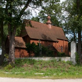 Zdjęcie nr 1: Kościół usytuowany na wzniesieniu, w otoczeniu bogatego drzewostanu. Orientowany, jednonawowy, z zamkniętym trójbocznie prezbiterium i przylegającą od północy zakrystią. Od południa i zachodu do korpusu przylegają kruchty. Nawa na planie prostokąta, szersza od prezbiterium. Wewnątrz pozorne sklepienie kolebkowe, w nawie z płaskimi odcinkami stropowymi po bokach, podpartymi na profilowanych słupach ustawionych na cokołach. Ściany opięte pilastrami naśladującymi formę słupów. Prezbiterium od korpusu oddziela łuk tęczowy, półkolisty, profilowany, ozdobiony ornamentem sznurowym, wsparty na profilowanych kroksztynach dekorowanych drewnianymi rozetami. Od zachodu parapet chóru muzycznego na planie prostokąta oparty na dwóch wielobocznych słupach, front dekorowany motywem w formie powtarzających się zwróconych do siebie par esownic i napisem „MIŁOŚCIĄ WIECZNĄ UMIŁOWAŁEM CIĘ” rozdzielonym wizerunkiem pelikana karmiącego młode własną krwią. Od południa schody prowadzące na chór z analogiczną dekoracją. Fasada prosta, zamknięta daszkiem krytym gontem, zwieńczona trójkątnie. Korpus z trzech stron wzmocniony belkami. Od strony północnej i południowej po dwa okna prostokątne zwieńczone niewielkimi blaszanymi daszkami. Prezbiterium od strony południowej opięte dwoma belkami, z prostokątnym oknem. Na ścianie wschodniej, na zewnątrz, kapliczka z ceramicznym przedstawieniem Matki Boskiej z Dzieciątkiem. W ścianach wschodniej i północnej zakrystii po jednym prostokątnym oknie. Dach dwuspadowy, o jednej kalenicy, od wschodu odzwierciedla układ ścian prezbiterium. Kruchty przykryte dachami dwuspadowymi. Dachy kryte gontem. Na przecięciu korpusu z prezbiterium blaszana, ośmioboczna wieżyczka na sygnaturkę zwieńczona hełmem baniastym ze spłaszczoną kulą z krzyżem. 