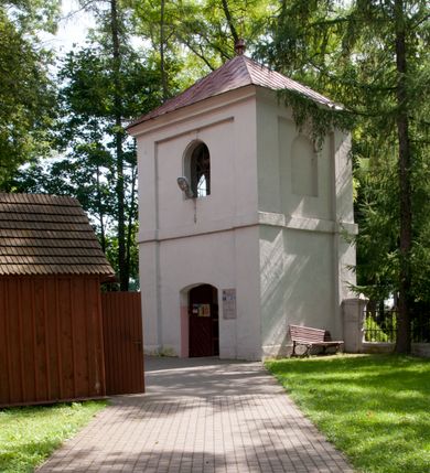 Zdjęcie nr 15: Kościół usytuowany na wzniesieniu, w otoczeniu bogatego drzewostanu. Orientowany, jednonawowy, z zamkniętym trójbocznie prezbiterium i przylegającą od północy zakrystią. Od południa i zachodu do korpusu przylegają kruchty. Nawa na planie prostokąta, szersza od prezbiterium. Wewnątrz pozorne sklepienie kolebkowe, w nawie z płaskimi odcinkami stropowymi po bokach, podpartymi na profilowanych słupach ustawionych na cokołach. Ściany opięte pilastrami naśladującymi formę słupów. Prezbiterium od korpusu oddziela łuk tęczowy, półkolisty, profilowany, ozdobiony ornamentem sznurowym, wsparty na profilowanych kroksztynach dekorowanych drewnianymi rozetami. Od zachodu parapet chóru muzycznego na planie prostokąta oparty na dwóch wielobocznych słupach, front dekorowany motywem w formie powtarzających się zwróconych do siebie par esownic i napisem „MIŁOŚCIĄ WIECZNĄ UMIŁOWAŁEM CIĘ” rozdzielonym wizerunkiem pelikana karmiącego młode własną krwią. Od południa schody prowadzące na chór z analogiczną dekoracją. Fasada prosta, zamknięta daszkiem krytym gontem, zwieńczona trójkątnie. Korpus z trzech stron wzmocniony belkami. Od strony północnej i południowej po dwa okna prostokątne zwieńczone niewielkimi blaszanymi daszkami. Prezbiterium od strony południowej opięte dwoma belkami, z prostokątnym oknem. Na ścianie wschodniej, na zewnątrz, kapliczka z ceramicznym przedstawieniem Matki Boskiej z Dzieciątkiem. W ścianach wschodniej i północnej zakrystii po jednym prostokątnym oknie. Dach dwuspadowy, o jednej kalenicy, od wschodu odzwierciedla układ ścian prezbiterium. Kruchty przykryte dachami dwuspadowymi. Dachy kryte gontem. Na przecięciu korpusu z prezbiterium blaszana, ośmioboczna wieżyczka na sygnaturkę zwieńczona hełmem baniastym ze spłaszczoną kulą z krzyżem. 