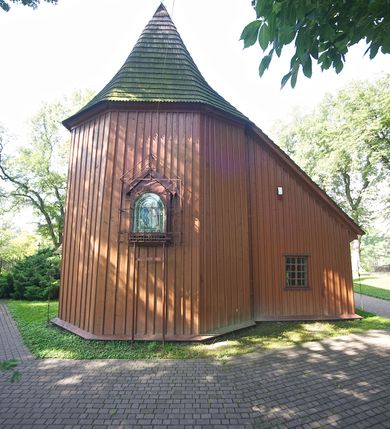 Zdjęcie nr 6: Kościół usytuowany na wzniesieniu, w otoczeniu bogatego drzewostanu. Orientowany, jednonawowy, z zamkniętym trójbocznie prezbiterium i przylegającą od północy zakrystią. Od południa i zachodu do korpusu przylegają kruchty. Nawa na planie prostokąta, szersza od prezbiterium. Wewnątrz pozorne sklepienie kolebkowe, w nawie z płaskimi odcinkami stropowymi po bokach, podpartymi na profilowanych słupach ustawionych na cokołach. Ściany opięte pilastrami naśladującymi formę słupów. Prezbiterium od korpusu oddziela łuk tęczowy, półkolisty, profilowany, ozdobiony ornamentem sznurowym, wsparty na profilowanych kroksztynach dekorowanych drewnianymi rozetami. Od zachodu parapet chóru muzycznego na planie prostokąta oparty na dwóch wielobocznych słupach, front dekorowany motywem w formie powtarzających się zwróconych do siebie par esownic i napisem „MIŁOŚCIĄ WIECZNĄ UMIŁOWAŁEM CIĘ” rozdzielonym wizerunkiem pelikana karmiącego młode własną krwią. Od południa schody prowadzące na chór z analogiczną dekoracją. Fasada prosta, zamknięta daszkiem krytym gontem, zwieńczona trójkątnie. Korpus z trzech stron wzmocniony belkami. Od strony północnej i południowej po dwa okna prostokątne zwieńczone niewielkimi blaszanymi daszkami. Prezbiterium od strony południowej opięte dwoma belkami, z prostokątnym oknem. Na ścianie wschodniej, na zewnątrz, kapliczka z ceramicznym przedstawieniem Matki Boskiej z Dzieciątkiem. W ścianach wschodniej i północnej zakrystii po jednym prostokątnym oknie. Dach dwuspadowy, o jednej kalenicy, od wschodu odzwierciedla układ ścian prezbiterium. Kruchty przykryte dachami dwuspadowymi. Dachy kryte gontem. Na przecięciu korpusu z prezbiterium blaszana, ośmioboczna wieżyczka na sygnaturkę zwieńczona hełmem baniastym ze spłaszczoną kulą z krzyżem. 