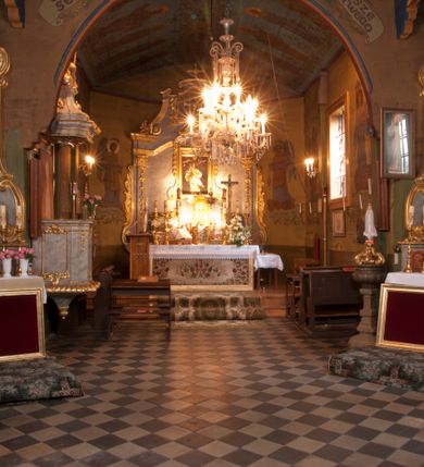 Zdjęcie nr 25: Kościół usytuowany na wzniesieniu, w otoczeniu bogatego drzewostanu. Orientowany, jednonawowy, z zamkniętym trójbocznie prezbiterium i przylegającą od północy zakrystią. Od południa i zachodu do korpusu przylegają kruchty. Nawa na planie prostokąta, szersza od prezbiterium. Wewnątrz pozorne sklepienie kolebkowe, w nawie z płaskimi odcinkami stropowymi po bokach, podpartymi na profilowanych słupach ustawionych na cokołach. Ściany opięte pilastrami naśladującymi formę słupów. Prezbiterium od korpusu oddziela łuk tęczowy, półkolisty, profilowany, ozdobiony ornamentem sznurowym, wsparty na profilowanych kroksztynach dekorowanych drewnianymi rozetami. Od zachodu parapet chóru muzycznego na planie prostokąta oparty na dwóch wielobocznych słupach, front dekorowany motywem w formie powtarzających się zwróconych do siebie par esownic i napisem „MIŁOŚCIĄ WIECZNĄ UMIŁOWAŁEM CIĘ” rozdzielonym wizerunkiem pelikana karmiącego młode własną krwią. Od południa schody prowadzące na chór z analogiczną dekoracją. Fasada prosta, zamknięta daszkiem krytym gontem, zwieńczona trójkątnie. Korpus z trzech stron wzmocniony belkami. Od strony północnej i południowej po dwa okna prostokątne zwieńczone niewielkimi blaszanymi daszkami. Prezbiterium od strony południowej opięte dwoma belkami, z prostokątnym oknem. Na ścianie wschodniej, na zewnątrz, kapliczka z ceramicznym przedstawieniem Matki Boskiej z Dzieciątkiem. W ścianach wschodniej i północnej zakrystii po jednym prostokątnym oknie. Dach dwuspadowy, o jednej kalenicy, od wschodu odzwierciedla układ ścian prezbiterium. Kruchty przykryte dachami dwuspadowymi. Dachy kryte gontem. Na przecięciu korpusu z prezbiterium blaszana, ośmioboczna wieżyczka na sygnaturkę zwieńczona hełmem baniastym ze spłaszczoną kulą z krzyżem. 