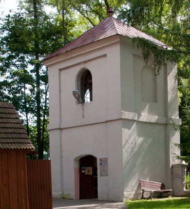 Zdjęcie nr 2: Dzwonnica murowana, tynkowana, dwukondygnacyjna, na planie kwadratu. Lico ścian opięte w narożach lizenami. W pierwszej kondygnacji przejście na przestrzał, w ścianach północnej i południowej otwory drzwiowe zamknięte łukiem odcinkowym – południowy dodatkowo zwieńczony niewielkim polem z plakietą. Kondygnacje zostały oddzielone od siebie prostym gzymsem. W drugiej, w każdej ścianie okno zamknięte półkoliście zwieńczone niewielką plakietą; od zachodu blenda. Kondygnację wieńczy gzyms. Całość przekryta dachem czterospadowym pokrytym blachą i zwieńczonym krzyżem.