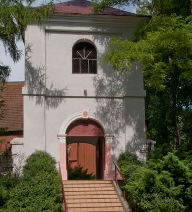 Zdjęcie nr 1: Dzwonnica murowana, tynkowana, dwukondygnacyjna, na planie kwadratu. Lico ścian opięte w narożach lizenami. W pierwszej kondygnacji przejście na przestrzał, w ścianach północnej i południowej otwory drzwiowe zamknięte łukiem odcinkowym – południowy dodatkowo zwieńczony niewielkim polem z plakietą. Kondygnacje zostały oddzielone od siebie prostym gzymsem. W drugiej, w każdej ścianie okno zamknięte półkoliście zwieńczone niewielką plakietą; od zachodu blenda. Kondygnację wieńczy gzyms. Całość przekryta dachem czterospadowym pokrytym blachą i zwieńczonym krzyżem.