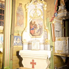 Zdjęcie nr 1: Ołtarz jednoosiowy, jednokondygnacyjny. Mensa w typie sarkofagowym, z krzyżem na ścianie frontowej. Na niej prostopadłościenne tabernakulum zamknięte od dołu i od góry gzymsem z krucyfiksem na drzwiczkach. Nastawa ołtarzowa na cokole o bokach dostawionych ukośnie, ujętych szerokimi taśmami o wolutowych zakończeniach i wspartymi na nich spływami. Górna część retabulum zwężająca się ku górze ujęta ceownicami i spływami wolutowymi o fantazyjnym kształcie. W polu nastawy obraz w kształcie stojącego prostokąta o ściętych narożach z przedstawieniem „Chrystusa z Samarytanką przy studni”. Powyżej obrazu dekoracja utworzona z dwóch karbowanych ceownic flankujących motyw koguciego grzebienia. Struktura marmoryzowana w odcieniach koloru szarego, profile i dekoracje złocone.