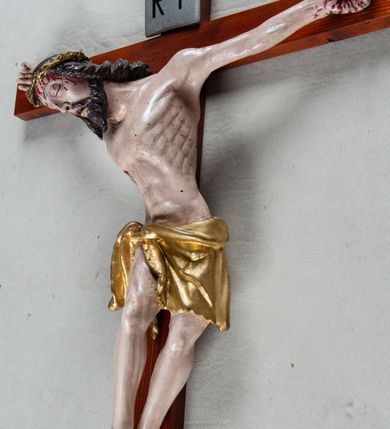 Zdjęcie nr 3: Pełnoplastyczna, polichromowana figura Chrystusa przybitego trzema gwoździami do krzyża łacińskiego. Ciało zmarłego odznacza się drobiazgowym opracowaniem anatomicznym, jest wygięte w łuk tak, że lewe biodro Chrystusa wychodzi poza oś. Na pociągłej twarzy są wyraźnie zaznaczone duże, zamknięte oczy, wąski, długi nos oraz rozchylone usta. Chrystus ma krótki zarost, długie, falowane, ciemnobrązowe włosy opadające na plecy i prawe ramię; na głowie złotą koronę cierniową, spod której spływają strużki krwi. Palce dłoni zwinięte, stopy przybite jednym gwoździem, prawa na lewej; z miejsc przebić oraz z przeciętego boku spływa krew. Wokół bioder owinięte sięgające kolan złote perizonium przewiązane sznurem na prawym biodrze. W dolnej partii pionowej belki srebrzony titulus w formie zwoju, z czarnym napisem „IN/RI”.