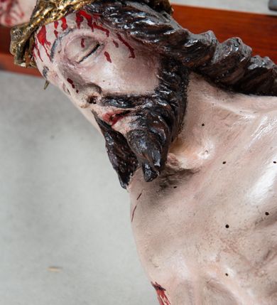 Zdjęcie nr 5: Pełnoplastyczna, polichromowana figura Chrystusa przybitego trzema gwoździami do krzyża łacińskiego. Ciało zmarłego odznacza się drobiazgowym opracowaniem anatomicznym, jest wygięte w łuk tak, że lewe biodro Chrystusa wychodzi poza oś. Na pociągłej twarzy są wyraźnie zaznaczone duże, zamknięte oczy, wąski, długi nos oraz rozchylone usta. Chrystus ma krótki zarost, długie, falowane, ciemnobrązowe włosy opadające na plecy i prawe ramię; na głowie złotą koronę cierniową, spod której spływają strużki krwi. Palce dłoni zwinięte, stopy przybite jednym gwoździem, prawa na lewej; z miejsc przebić oraz z przeciętego boku spływa krew. Wokół bioder owinięte sięgające kolan złote perizonium przewiązane sznurem na prawym biodrze. W dolnej partii pionowej belki srebrzony titulus w formie zwoju, z czarnym napisem „IN/RI”.