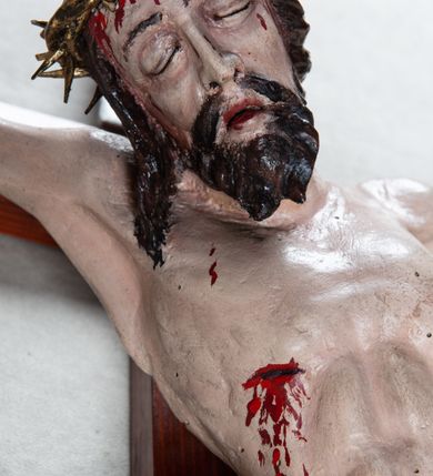 Zdjęcie nr 4: Pełnoplastyczna, polichromowana figura Chrystusa przybitego trzema gwoździami do krzyża łacińskiego. Ciało zmarłego odznacza się drobiazgowym opracowaniem anatomicznym, jest wygięte w łuk tak, że lewe biodro Chrystusa wychodzi poza oś. Na pociągłej twarzy są wyraźnie zaznaczone duże, zamknięte oczy, wąski, długi nos oraz rozchylone usta. Chrystus ma krótki zarost, długie, falowane, ciemnobrązowe włosy opadające na plecy i prawe ramię; na głowie złotą koronę cierniową, spod której spływają strużki krwi. Palce dłoni zwinięte, stopy przybite jednym gwoździem, prawa na lewej; z miejsc przebić oraz z przeciętego boku spływa krew. Wokół bioder owinięte sięgające kolan złote perizonium przewiązane sznurem na prawym biodrze. W dolnej partii pionowej belki srebrzony titulus w formie zwoju, z czarnym napisem „IN/RI”.