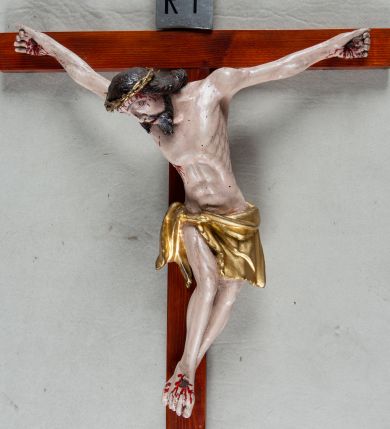 Zdjęcie nr 1: Pełnoplastyczna, polichromowana figura Chrystusa przybitego trzema gwoździami do krzyża łacińskiego. Ciało zmarłego odznacza się drobiazgowym opracowaniem anatomicznym, jest wygięte w łuk tak, że lewe biodro Chrystusa wychodzi poza oś. Na pociągłej twarzy są wyraźnie zaznaczone duże, zamknięte oczy, wąski, długi nos oraz rozchylone usta. Chrystus ma krótki zarost, długie, falowane, ciemnobrązowe włosy opadające na plecy i prawe ramię; na głowie złotą koronę cierniową, spod której spływają strużki krwi. Palce dłoni zwinięte, stopy przybite jednym gwoździem, prawa na lewej; z miejsc przebić oraz z przeciętego boku spływa krew. Wokół bioder owinięte sięgające kolan złote perizonium przewiązane sznurem na prawym biodrze. W dolnej partii pionowej belki srebrzony titulus w formie zwoju, z czarnym napisem „IN/RI”.