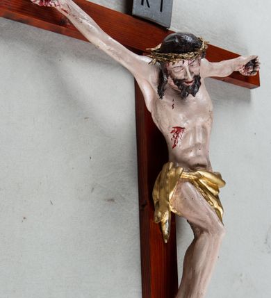 Zdjęcie nr 2: Pełnoplastyczna, polichromowana figura Chrystusa przybitego trzema gwoździami do krzyża łacińskiego. Ciało zmarłego odznacza się drobiazgowym opracowaniem anatomicznym, jest wygięte w łuk tak, że lewe biodro Chrystusa wychodzi poza oś. Na pociągłej twarzy są wyraźnie zaznaczone duże, zamknięte oczy, wąski, długi nos oraz rozchylone usta. Chrystus ma krótki zarost, długie, falowane, ciemnobrązowe włosy opadające na plecy i prawe ramię; na głowie złotą koronę cierniową, spod której spływają strużki krwi. Palce dłoni zwinięte, stopy przybite jednym gwoździem, prawa na lewej; z miejsc przebić oraz z przeciętego boku spływa krew. Wokół bioder owinięte sięgające kolan złote perizonium przewiązane sznurem na prawym biodrze. W dolnej partii pionowej belki srebrzony titulus w formie zwoju, z czarnym napisem „IN/RI”.