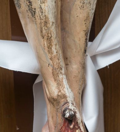 Zdjęcie nr 5: Pełnoplastyczna, polichromowana figura Chrystusa przybitego do krzyża. Ciało o jasnej karnacji i drobiazgowo opracowanej anatomii. Głowa pochylona w dół, lekko w prawo. Twarz owalna o łagodnych rysach, z zamkniętymi, otoczonymi fioletowym cieniem oczami, wąskim nosie i zamkniętych, sinych ustach; z krótkim, brązowym zarostem. Włosy długie, falowane, jasnobrązowe, opadające na plecy i prawe ramię. Na głowie korona cierniowa. Ramiona rozłożone, w prawym boku rana. Nogi wyprostowane, przebite jednym gwoździem, prawa na lewej. Na biodrach krótkie, złote, silnie drapowane, przewiązane na lewym biodrze perizonium, rozwiewające się gęstymi, łamanymi fałdami na wysokości uda w lewą stronę. W środkowej partii pionowej belki biały titulus w formie zwoju z czarnym napisem „INRI”.