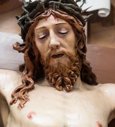 Zdjęcie nr 4: Pełnoplastyczna, polichromowana figura Chrystusa przybitego do krzyża. Ciało o jasnej karnacji i drobiazgowo opracowanej anatomii. Głowa pochylona w dół, lekko w prawo. Twarz owalna o łagodnych rysach, z zamkniętymi, otoczonymi fioletowym cieniem oczami, wąskim nosie i zamkniętych, sinych ustach; z krótkim, brązowym zarostem. Włosy długie, falowane, jasnobrązowe, opadające na plecy i prawe ramię. Na głowie korona cierniowa. Ramiona rozłożone, w prawym boku rana. Nogi wyprostowane, przebite jednym gwoździem, prawa na lewej. Na biodrach krótkie, złote, silnie drapowane, przewiązane na lewym biodrze perizonium, rozwiewające się gęstymi, łamanymi fałdami na wysokości uda w lewą stronę. W środkowej partii pionowej belki biały titulus w formie zwoju z czarnym napisem „INRI”.