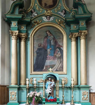Zdjęcie nr 1: Ołtarz architektoniczny, jednokondygnacyjny, jednoosiowy ze zwieńczeniem. Nastawa na pięciodzielnym cokole o uskokowych bokach. Pierwsza kondygnacja retabulum ujęta dwoma parami kolumn o kanelowanych trzonach i korynckich kapitelach, z których przednie wysunięte na zewnątrz wspierają przerwane, wyłamujące się ponad nimi belkowanie z silnie wysuniętym gzymsem. Pole środkowe wypełnia rama w kształcie stojącego prostokąta zamkniętego łukiem półkolistym z obrazem Matki Boskiej Różańcowej, ponad którą uskrzydlona głowa aniołka. Zwieńczenie retabulum o wklęsłych bokach ujęte parą spływów wolutowych, zamknięte odcinkiem gzymsu w formie łuku odcinkowego nadwieszonego, flankowane odcinkami przerwanego, wklęsło-wypukłego naczółka. Pole zwieńczenia w kształcie stojącego owalu z przedstawieniem Ecce Homo, poniżej którego dwie uskrzydlone główki anielskie. Na fragmentach przyczółka para siedzących aniołków. Szczyt w formie promienistej glorii z monogramem maryjnym na tle srebrzonych obłoków flankowany parą płonących wazonów. 
Retabulum zdobione ornamentyką roślinną z motywem wici w dolnej partii, akantu wokół ram obrazowych, rozetek na fryzie i kampanul wypełniających spływy. 
Struktura polichromowana w odcieniach zieleni. Detal architektoniczny i ornamentyka złocone i srebrzone. Aniołki polichromowane naturalistycznie. 
