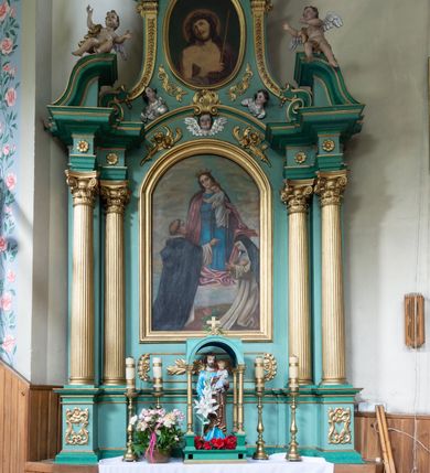 Zdjęcie nr 2: Ołtarz architektoniczny, jednokondygnacyjny, jednoosiowy ze zwieńczeniem. Nastawa na pięciodzielnym cokole o uskokowych bokach. Pierwsza kondygnacja retabulum ujęta dwoma parami kolumn o kanelowanych trzonach i korynckich kapitelach, z których przednie wysunięte na zewnątrz wspierają przerwane, wyłamujące się ponad nimi belkowanie z silnie wysuniętym gzymsem. Pole środkowe wypełnia rama w kształcie stojącego prostokąta zamkniętego łukiem półkolistym z obrazem Matki Boskiej Różańcowej, ponad którą uskrzydlona głowa aniołka. Zwieńczenie retabulum o wklęsłych bokach ujęte parą spływów wolutowych, zamknięte odcinkiem gzymsu w formie łuku odcinkowego nadwieszonego, flankowane odcinkami przerwanego, wklęsło-wypukłego naczółka. Pole zwieńczenia w kształcie stojącego owalu z przedstawieniem Ecce Homo, poniżej którego dwie uskrzydlone główki anielskie. Na fragmentach przyczółka para siedzących aniołków. Szczyt w formie promienistej glorii z monogramem maryjnym na tle srebrzonych obłoków flankowany parą płonących wazonów. 
Retabulum zdobione ornamentyką roślinną z motywem wici w dolnej partii, akantu wokół ram obrazowych, rozetek na fryzie i kampanul wypełniających spływy. 
Struktura polichromowana w odcieniach zieleni. Detal architektoniczny i ornamentyka złocone i srebrzone. Aniołki polichromowane naturalistycznie. 
