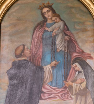 Zdjęcie nr 1: Obraz z przedstawieniem tronującej Matki Boskiej z Dzieciątkiem, przekazujących różańce klęczącym przed nimi 
 – św. Dominikowi i św. Katarzynie Sieneńskiej. Maria siedzi, spogląda delikatnie w dół. Na jej lewym kolanie stoi Dzieciątko, które podtrzymuje prawą ręką, lewą przekazując różaniec świętej. Maria ma trójkątną twarz z ciemnymi, otoczonymi cieniami oczami, wąskim nosem oraz małymi ustami. Jest ubrana w niebieską suknię oraz różowy, opadający drobnymi kaskadami na boki płaszcz, który fałduje się obficie pod jej stopami. Na głowie ma zdobioną drogimi kamieniami koronę. Dzieciątko spogląda na św. Dominika, prawą rękę wyciąga w jego kierunku w geście błogosławieństwa, lewą podaje mu różaniec. Ma okrągłą twarz, ciemne oczy, mały nos i usta, nieznacznie się uśmiecha. Jest ubrane w białą, długą sukienkę. Po lewej stronie przedstawienia klęczy św. Dominik, który spogląda na Dzieciątko i prawą ręką odbiera od niego różaniec. Ubrany jest w biały habit i czarny płaszcz zakonny, na głowie ma wyciętą tonsurę. Klęcząca po prawej stronie św. Katarzyna patrzy na podtrzymywany lewą ręką różaniec, prawą składa na piersi. Ubrana jest w biały habit i czarny płaszcz, na głowie ma koronę cierniową. Scena rozgrywa się na tle niebieskiego nieba przykrytego gęsto żółtopomarańczowymi chmurami. Między klęczącymi świętymi wyrasta z ziemi kwitnący krzew różany.
